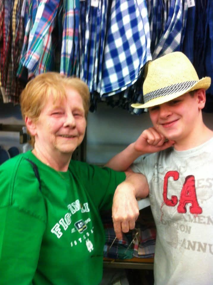 A young man and an older woman smile together while trying on hats in a clothing store.