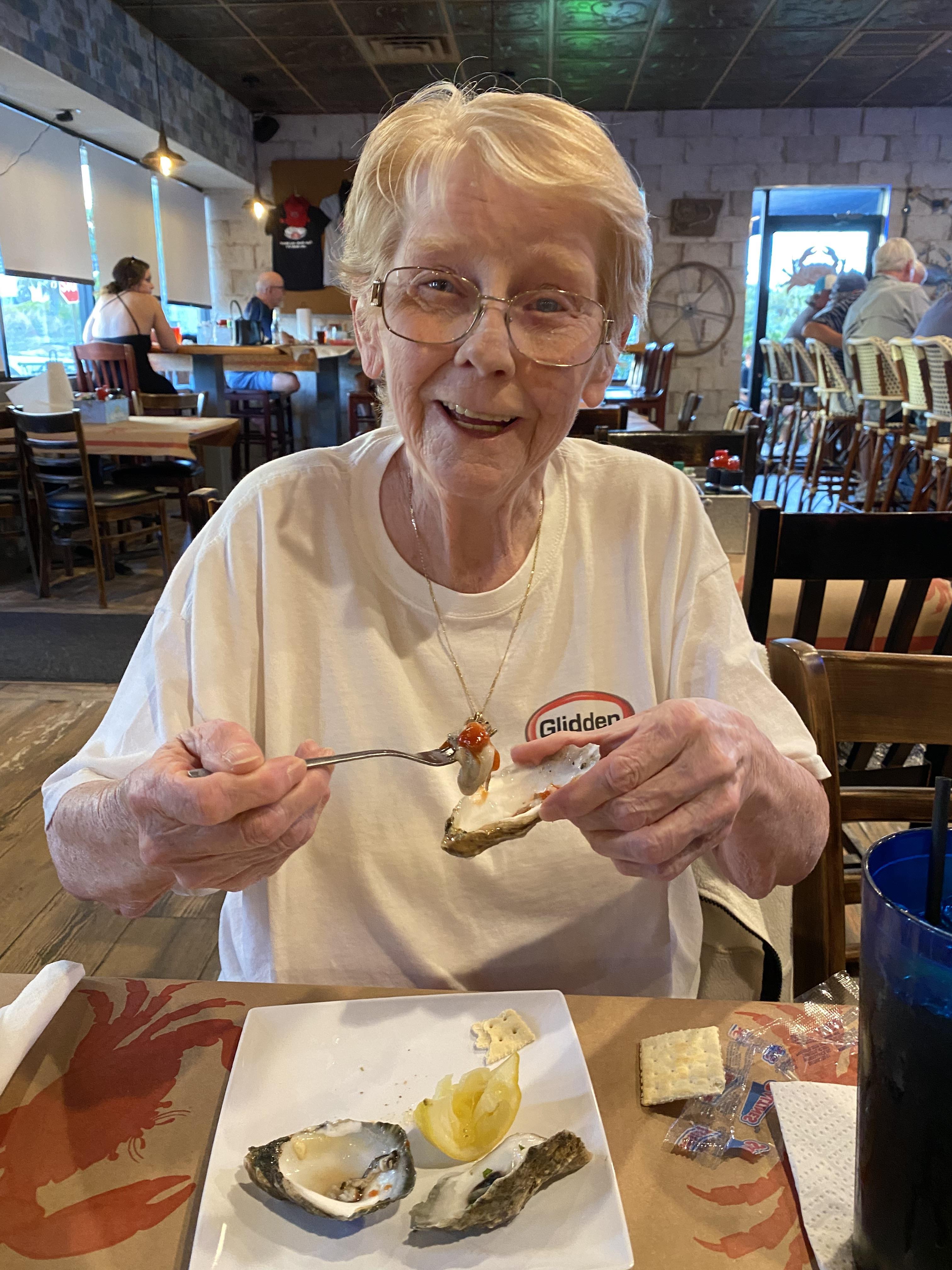 Elderly woman smiling while enjoying food at a relaxed dining establishment during lunch.