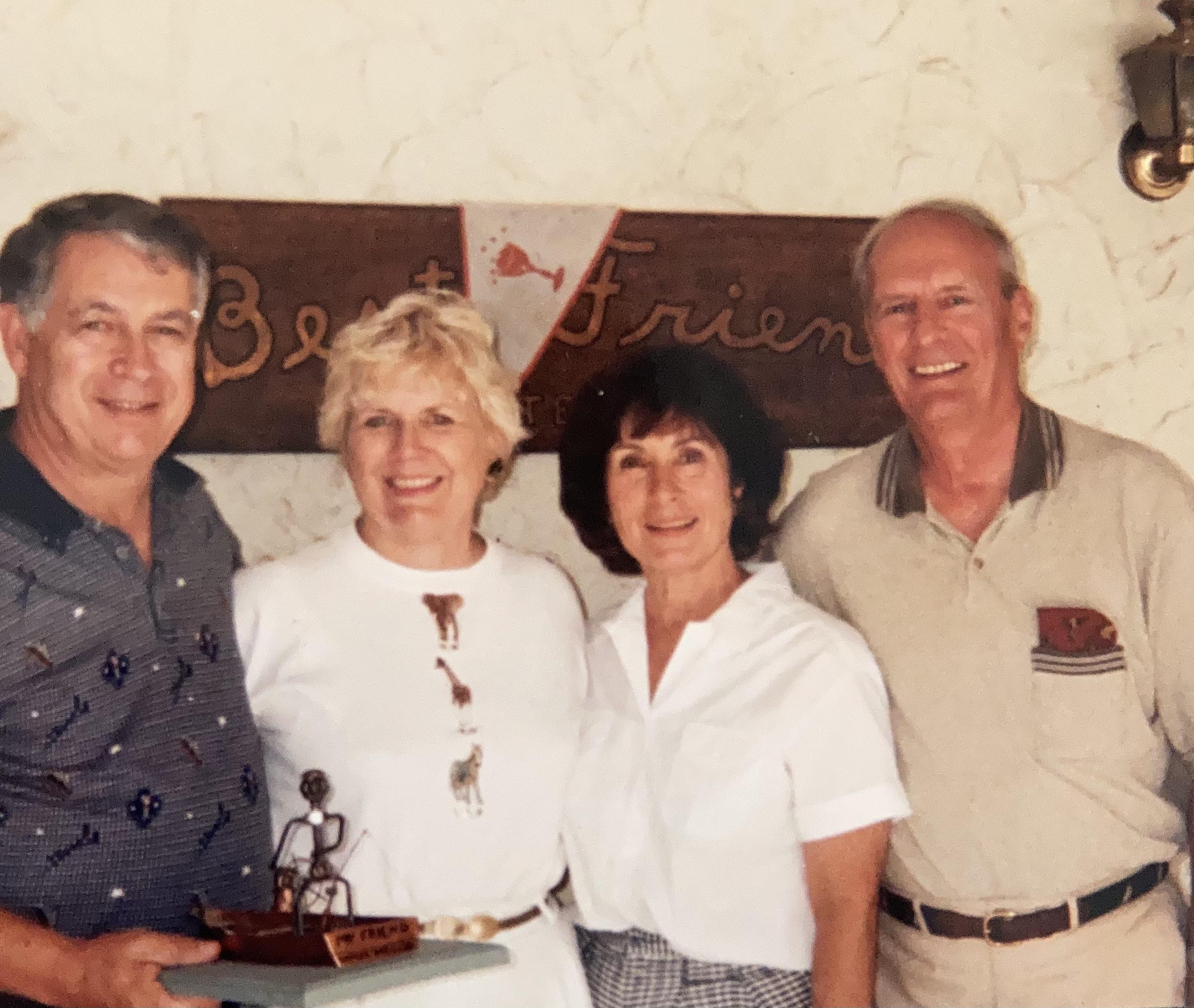 Four friends pose together, holding a trophy, smiling joyfully at a coastal gathering.