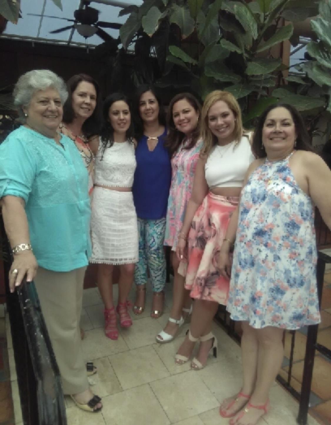 Women joyfully gather, smiling and posing in colorful outfits against a bright backdrop.