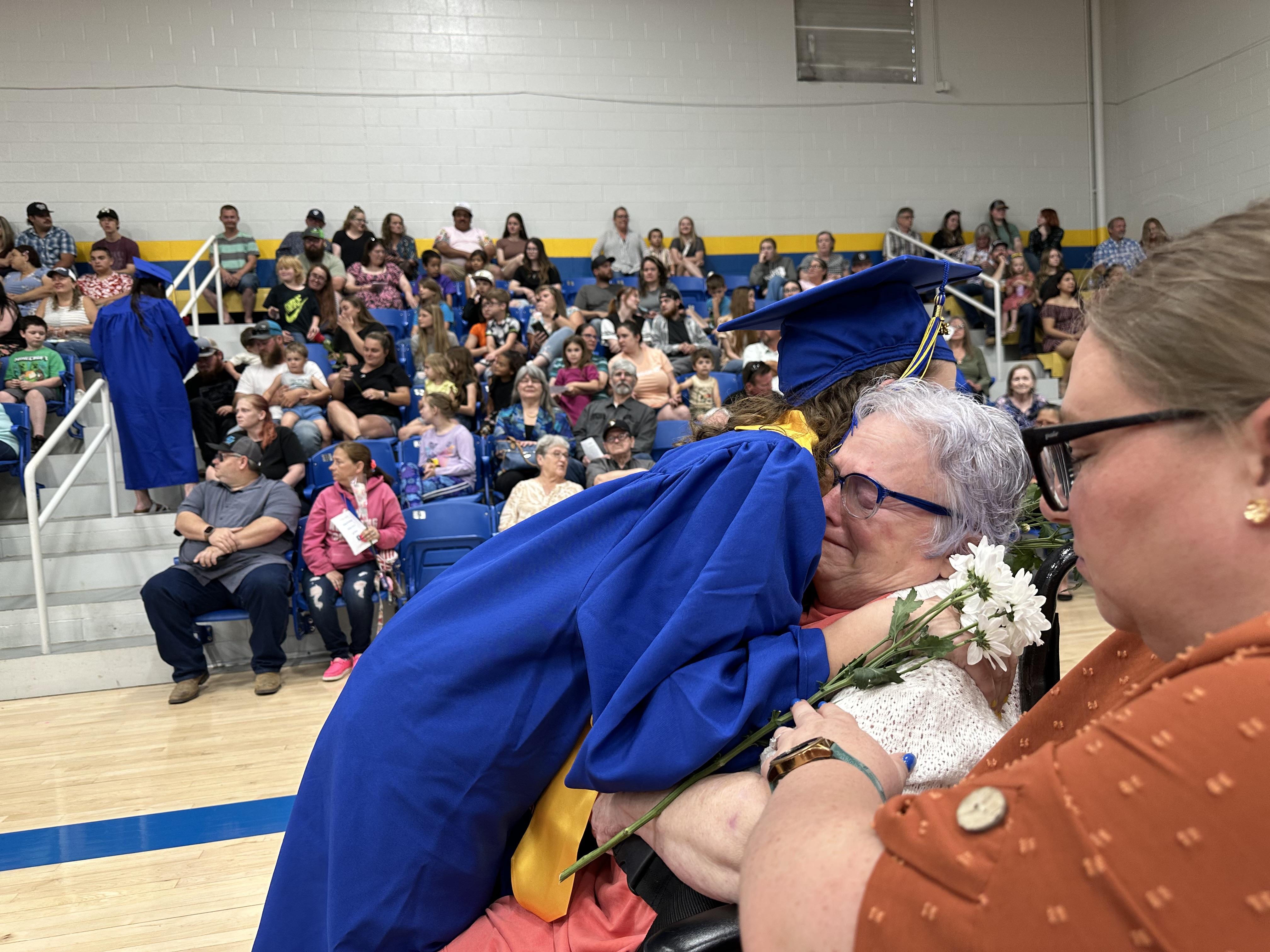 A graduate hugs her grandmother as others celebrate in the background at the ceremony.