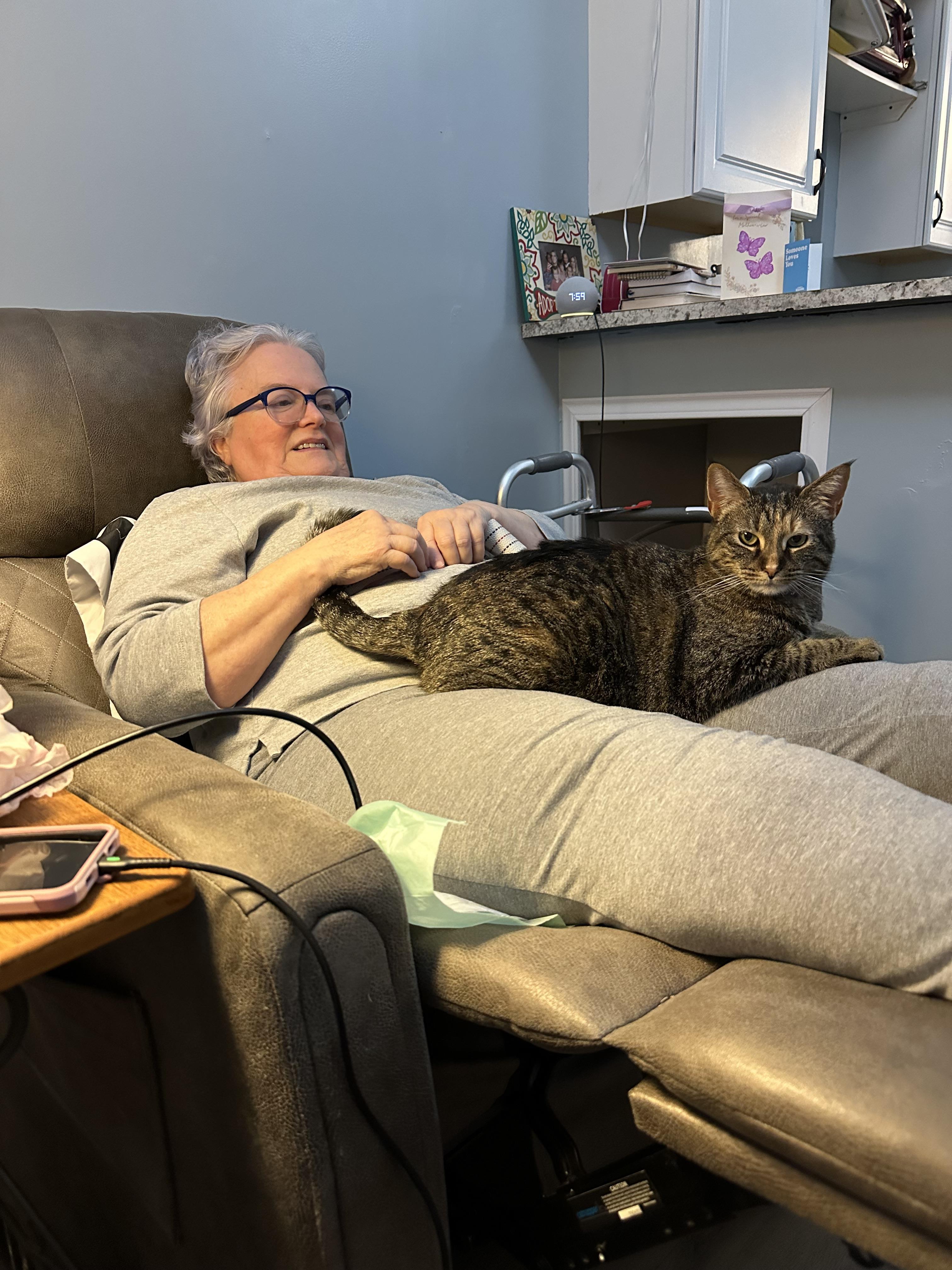 An elderly woman enjoys a peaceful moment with her gray cat resting on her lap at home.