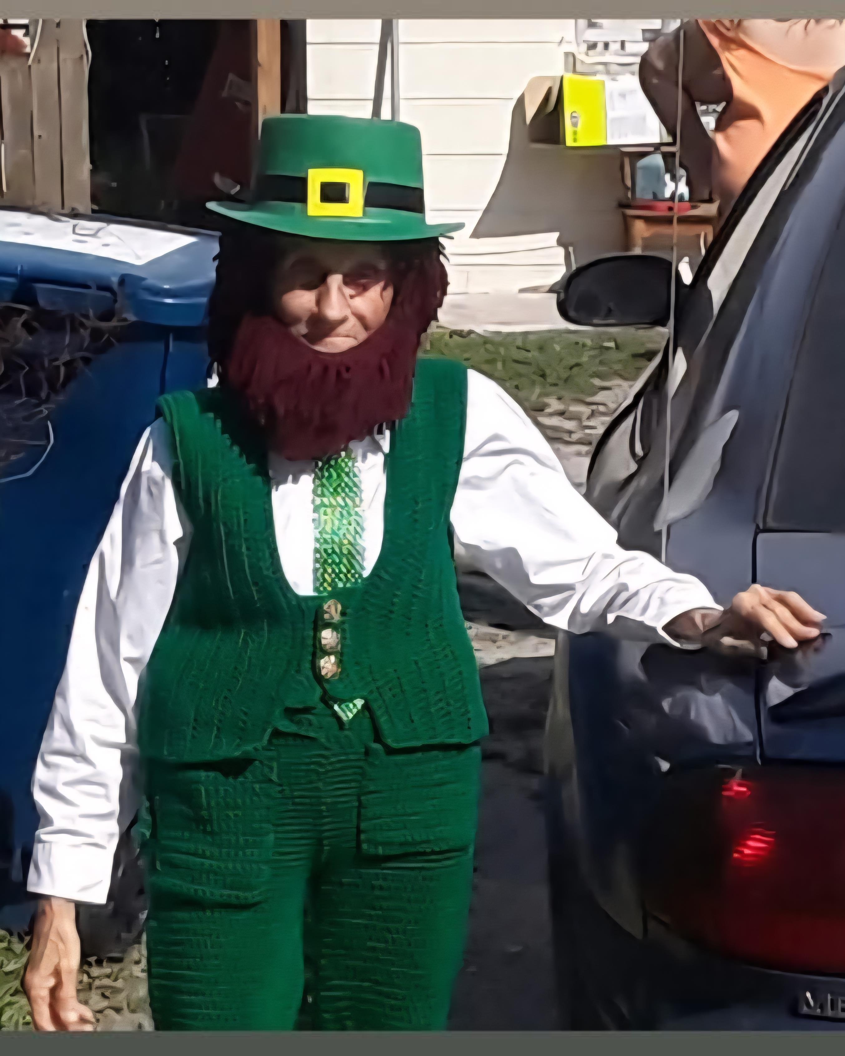 A person dressed as a leprechaun poses in a colorful costume against a sunny backdrop.