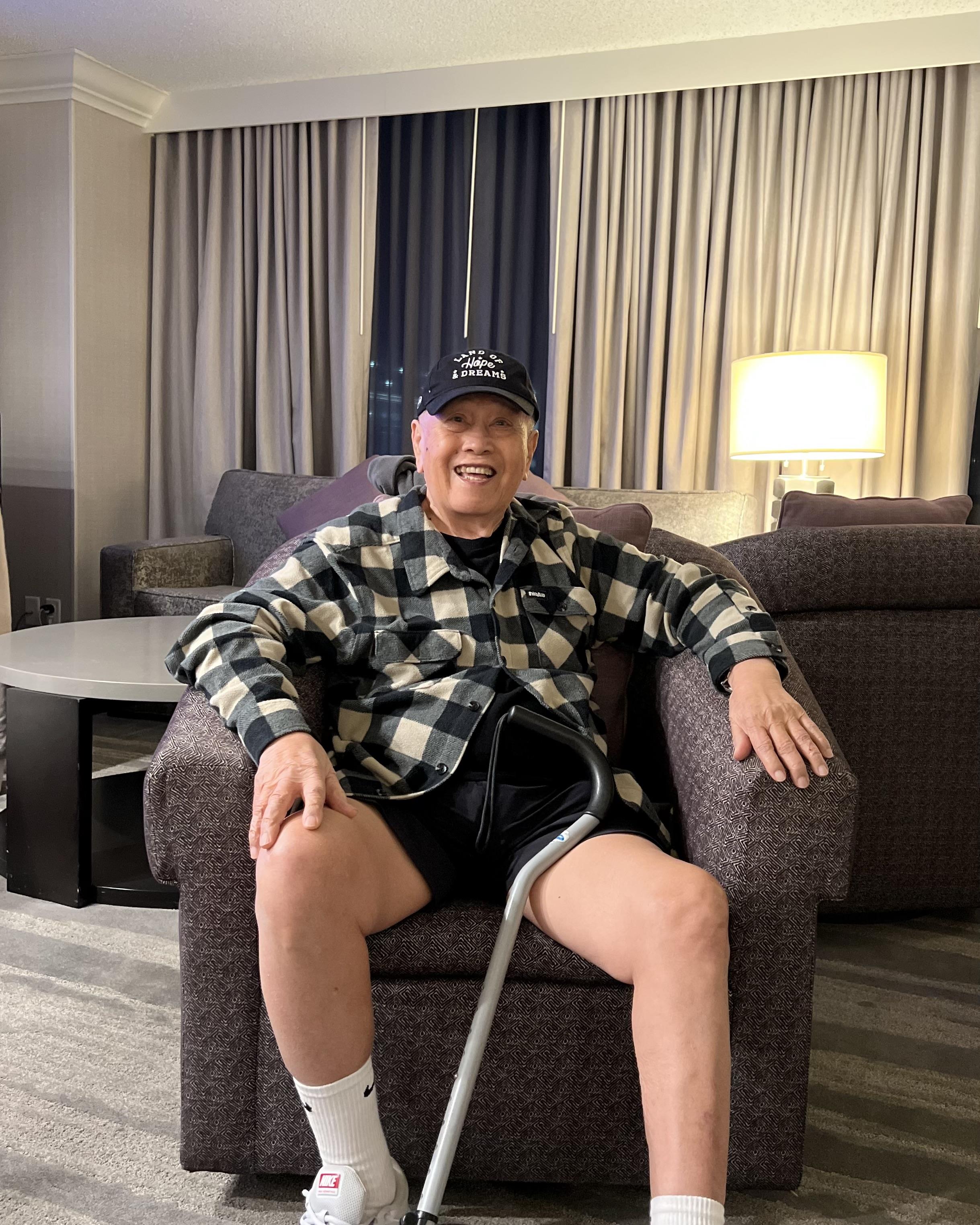 An elderly man enjoys his time sitting comfortably in a hotel lounge chair, smiling and relaxed.