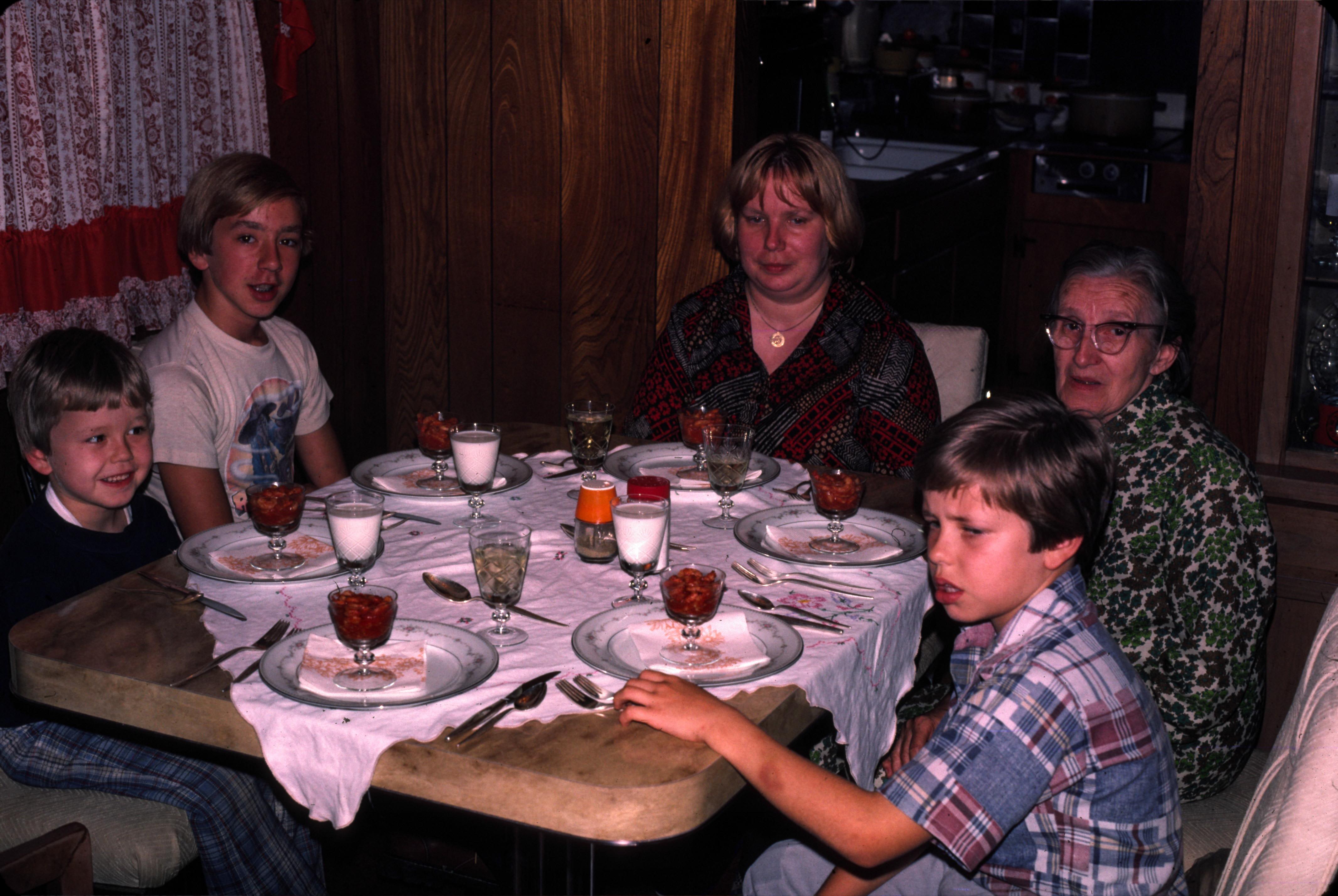 Five family members sit together at a table with dessert and drinks, sharing a joyful moment.