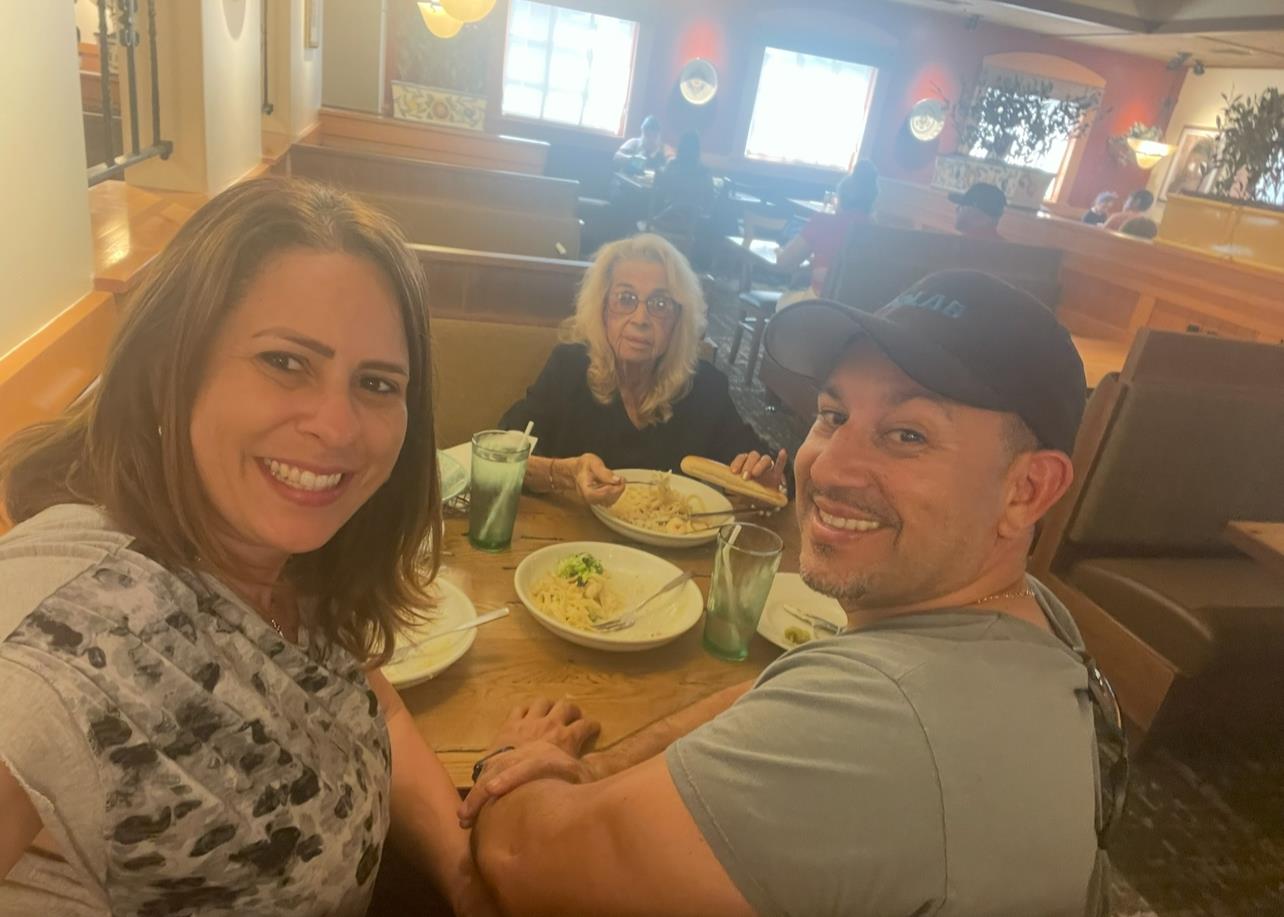 Three people are seated at a table, sharing a meal and smiling, creating a joyful atmosphere.