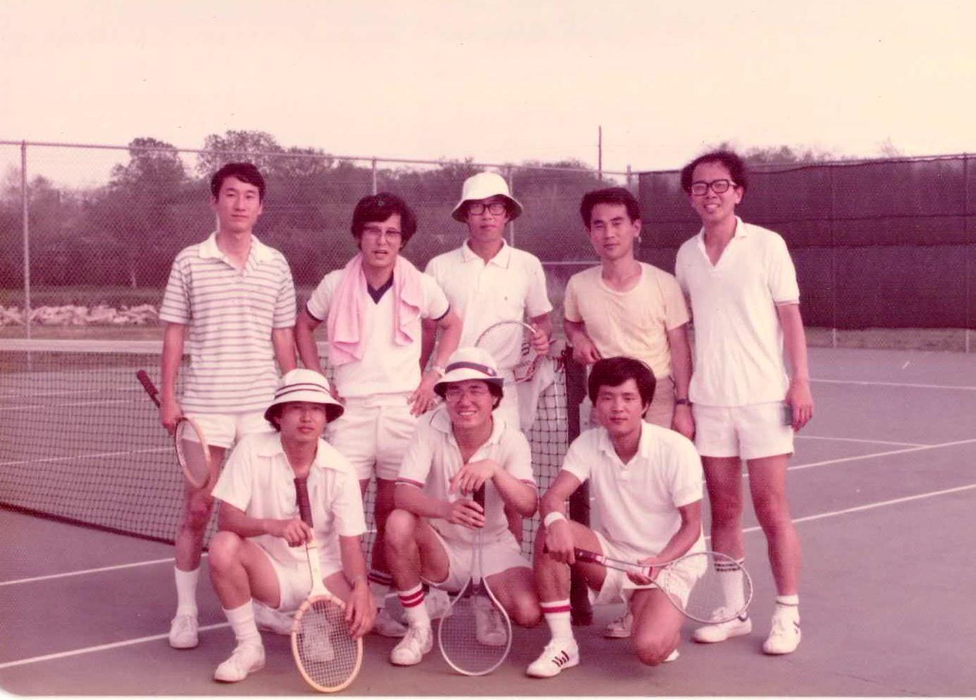 Eight friends gather at a tennis court, ready for a fun game in warm weather while smiling.