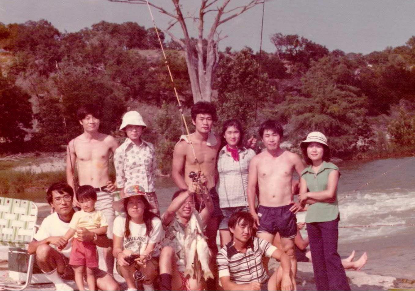 Friends gather for a summer fishing trip, showcasing their catches near the riverbank.