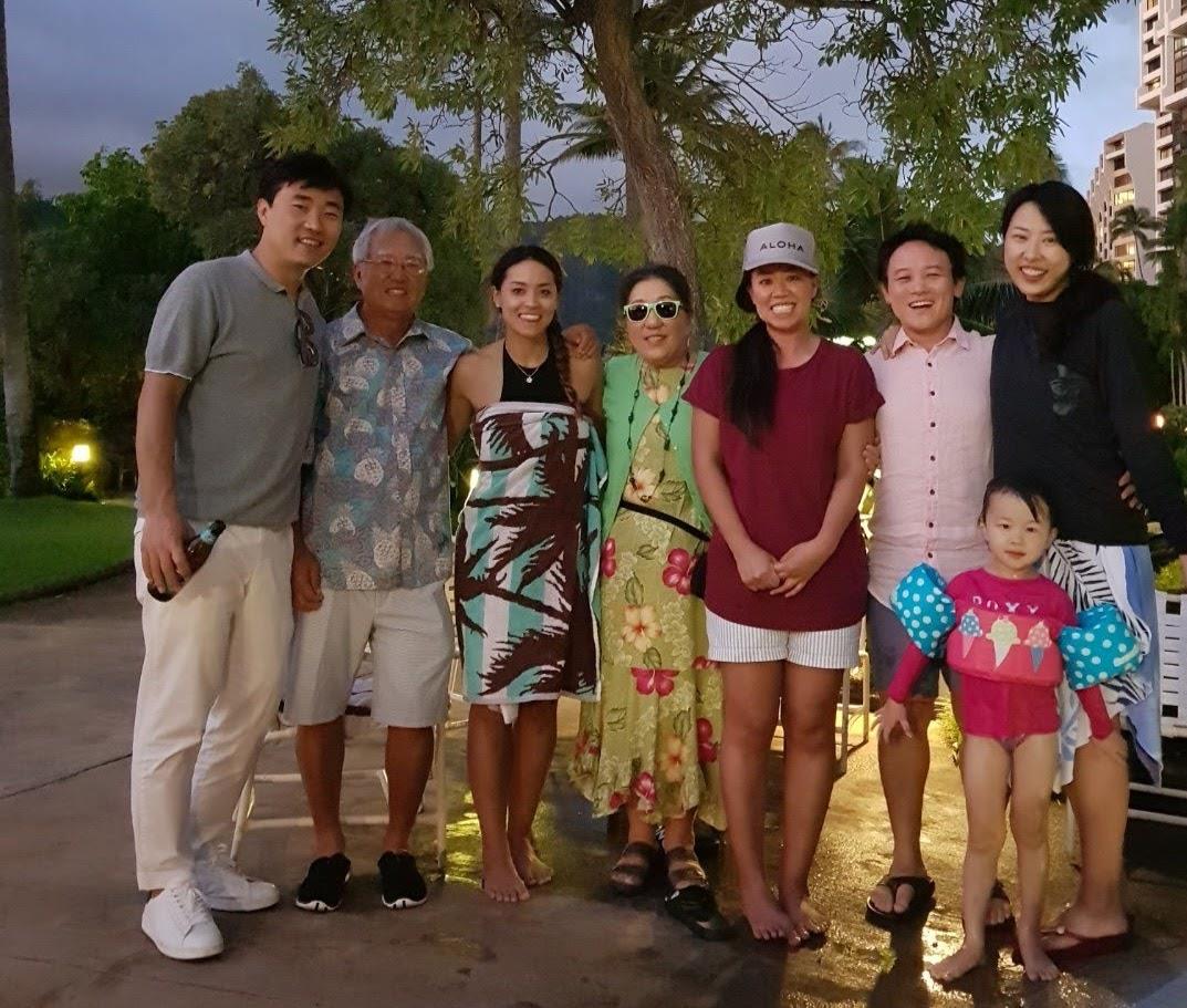 A joyful family gathering near a garden at sunset, showing diverse outfits and smiles.