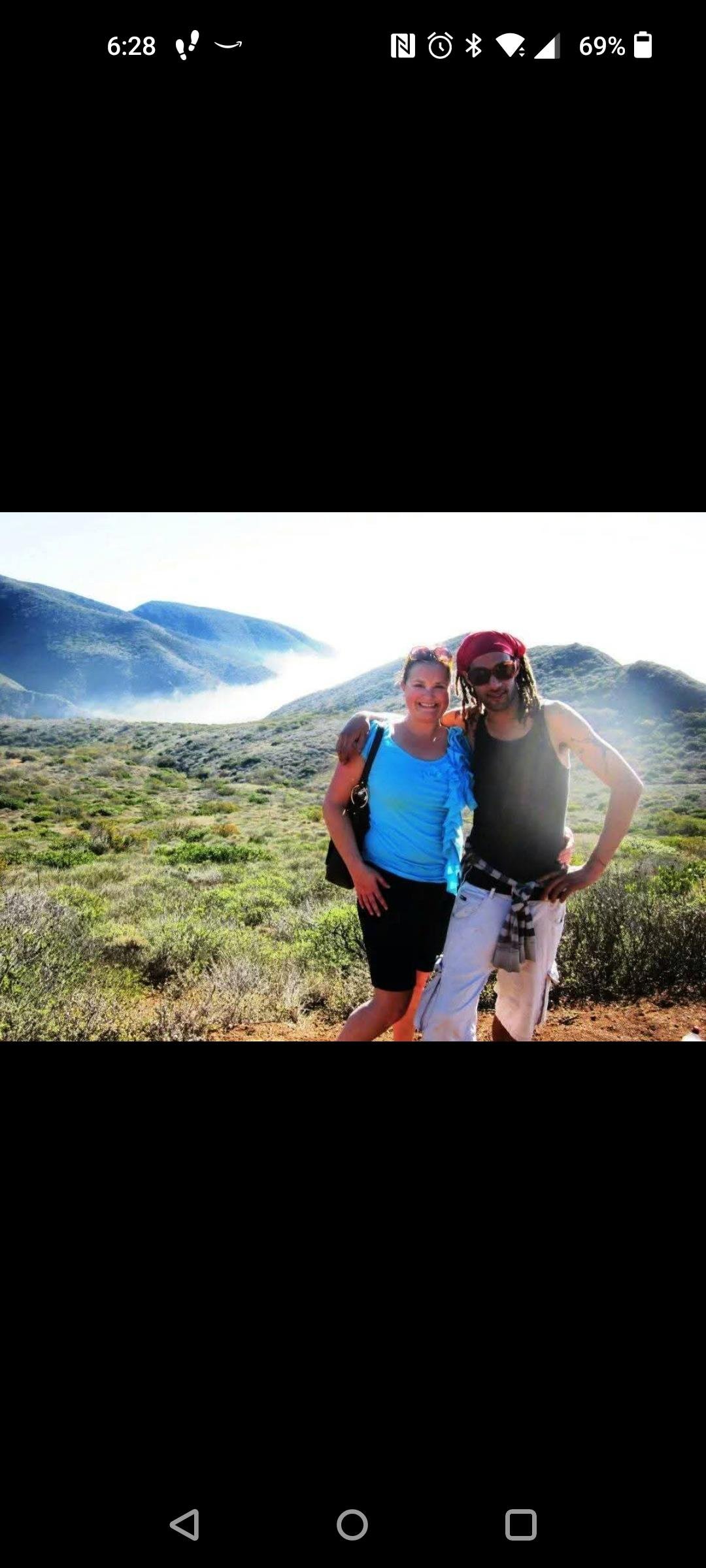 Two hikers pose against a breathtaking landscape with hills and distant mountains.