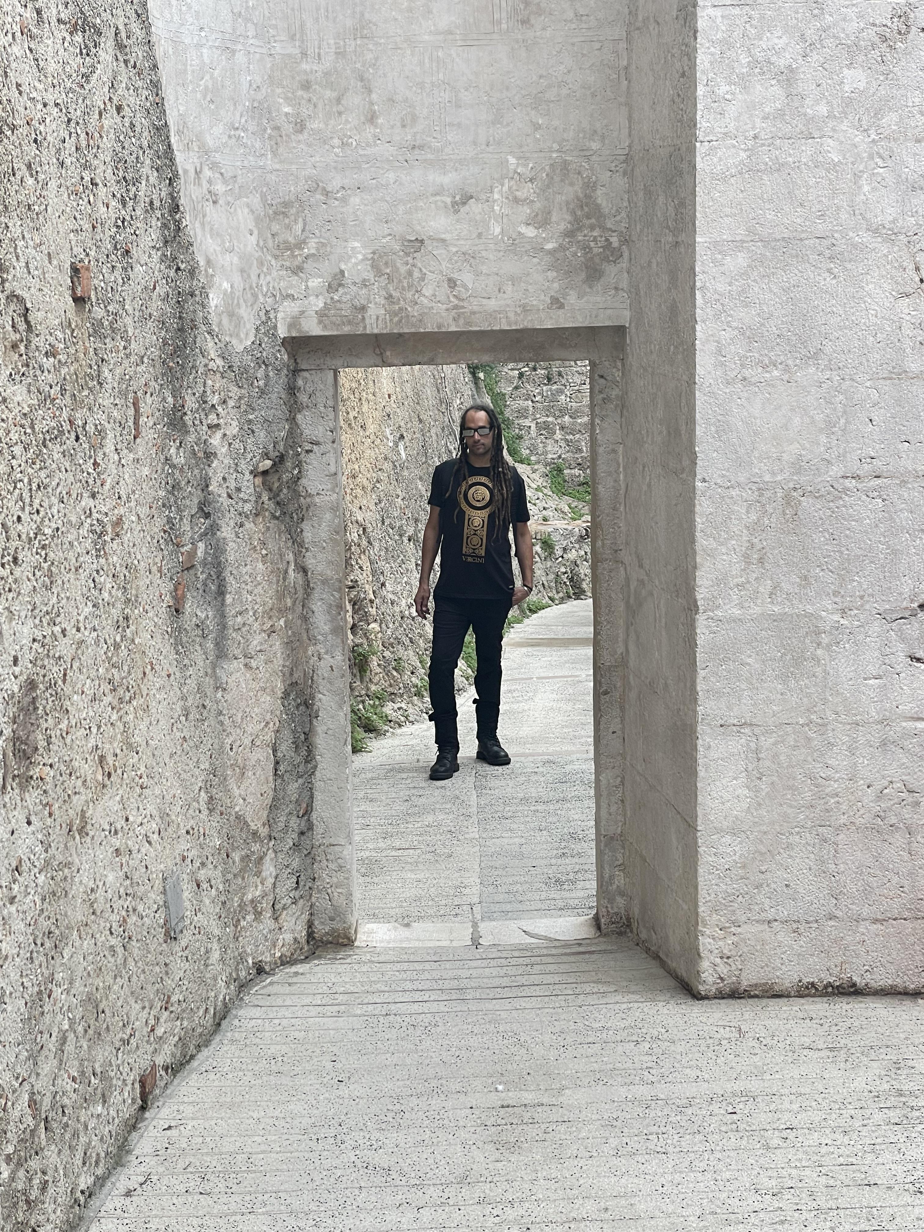A person is positioned in a narrow corridor made of stone, surrounded by historic walls.