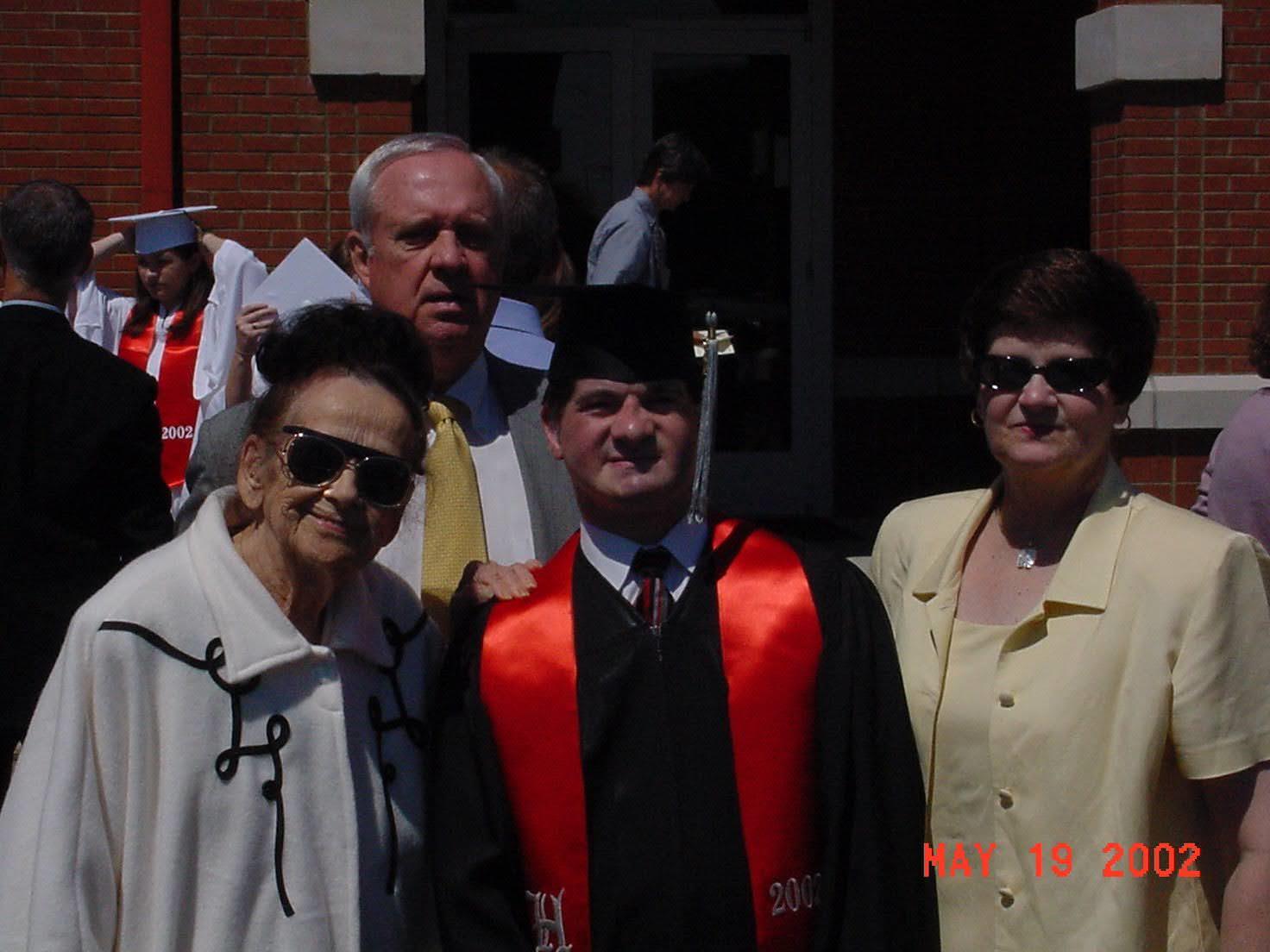 A proud graduate stands alongside family members outside a school after the ceremony.