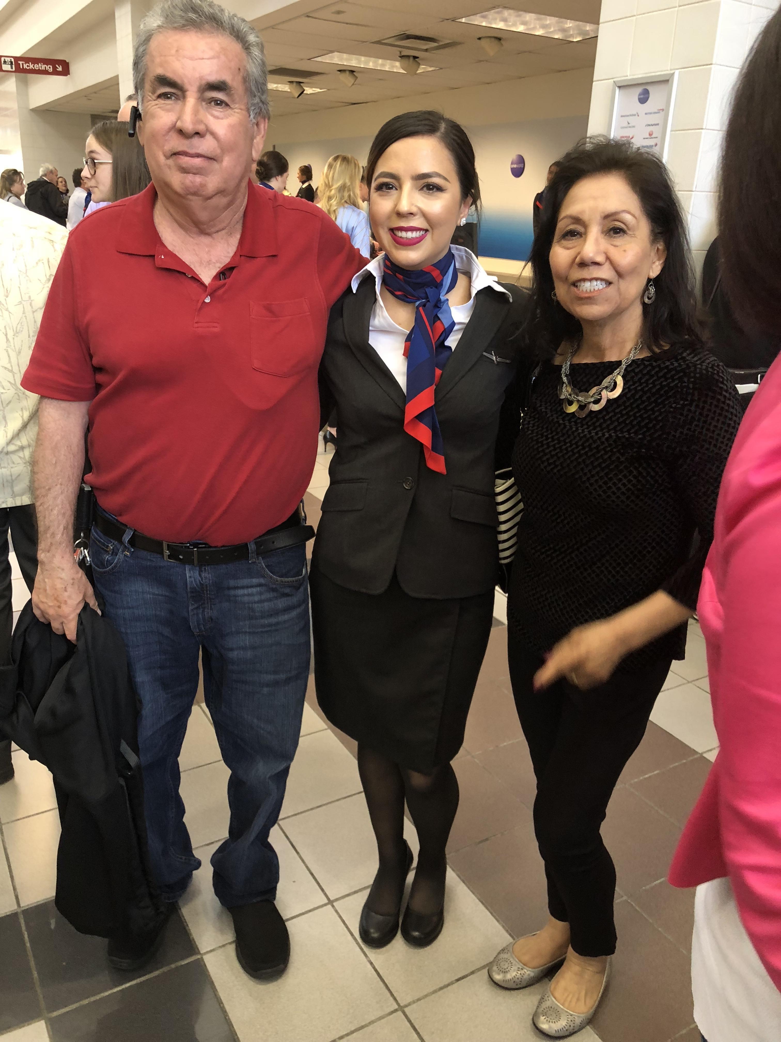 A flight attendant happily poses with her parents in an airport terminal.