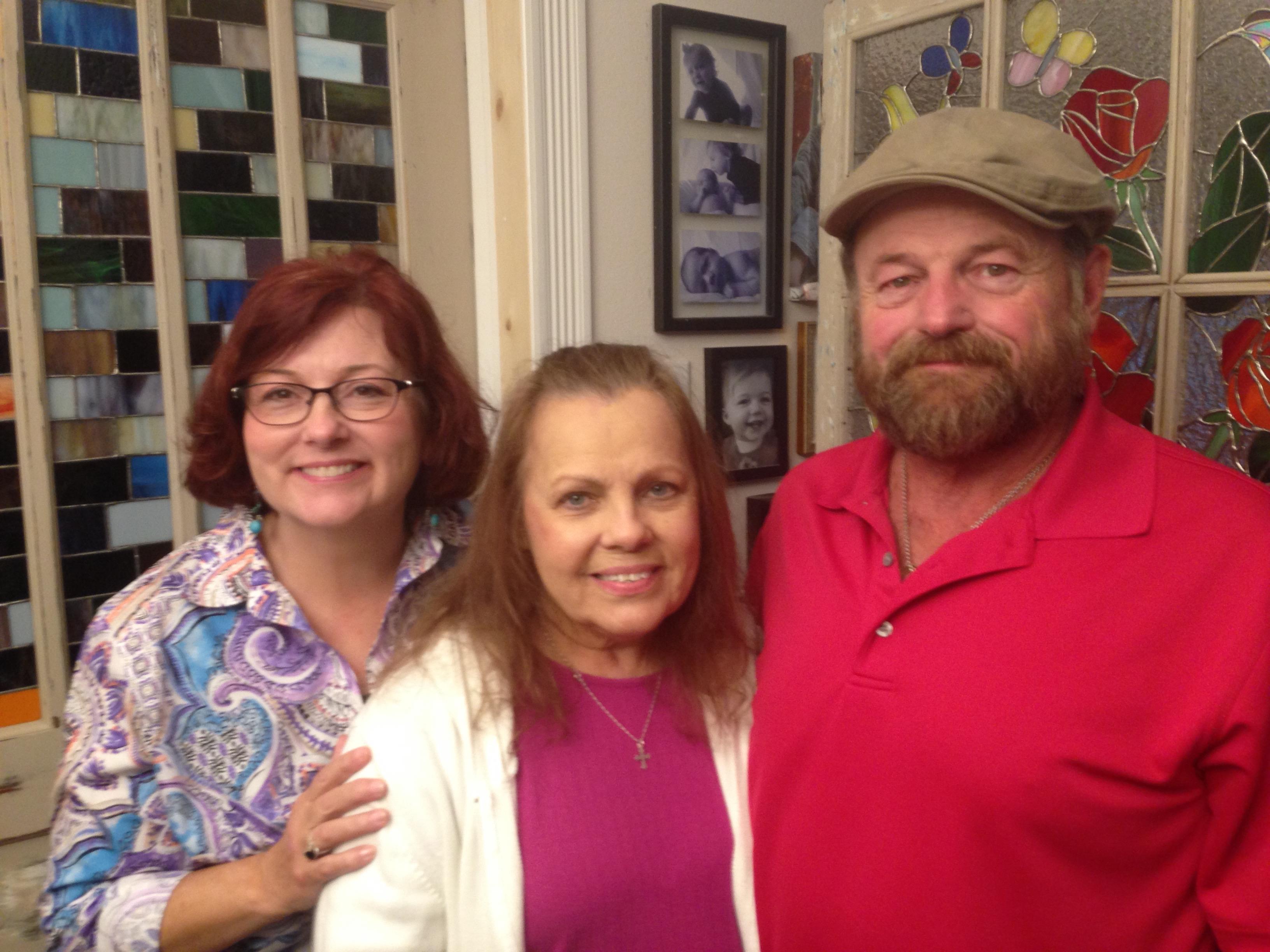 Three friends pose together, smiling warmly in a brightly decorated room filled with memories.