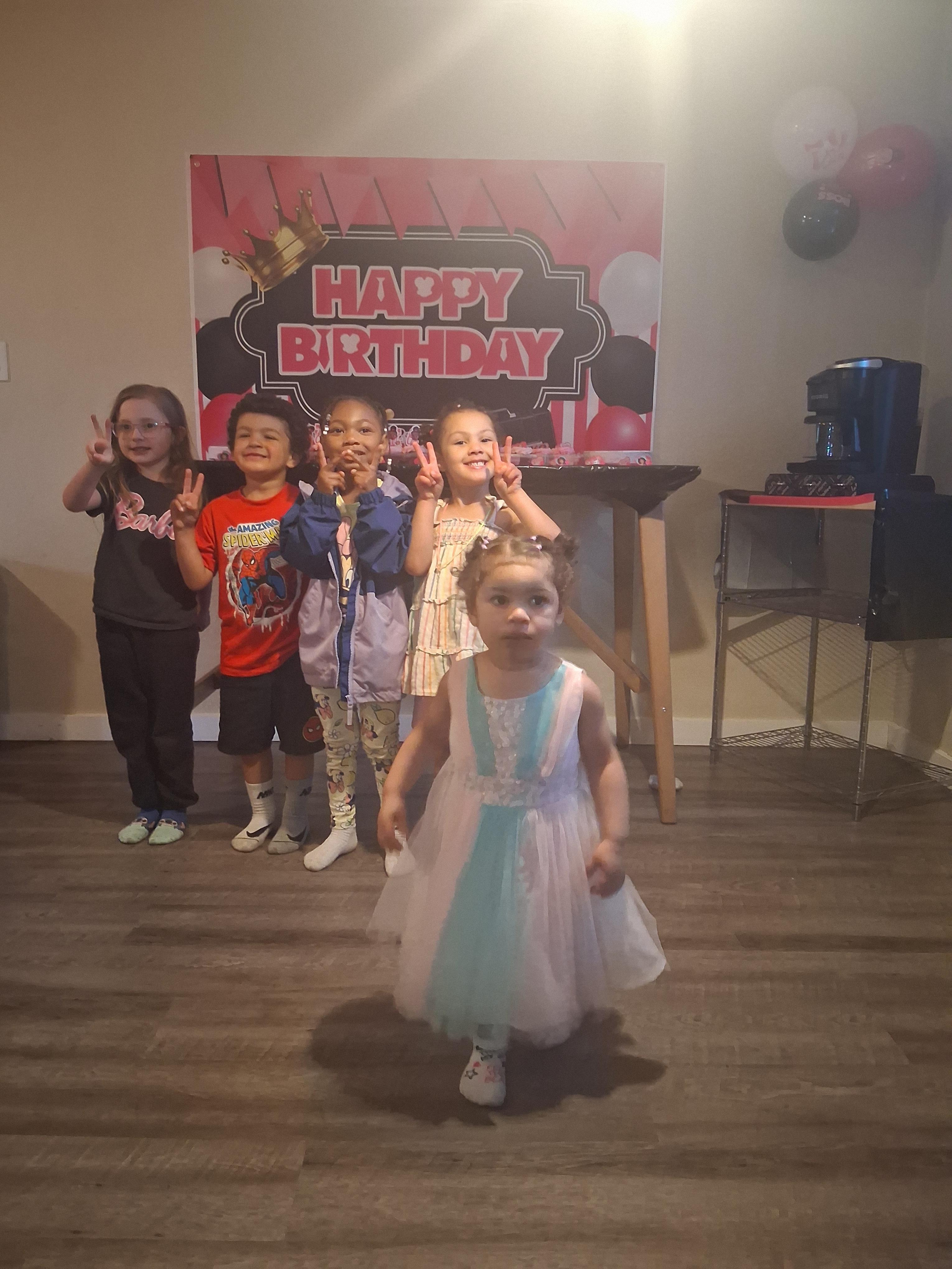 Kids gather in a bright room, posing happily for a birthday celebration with colorful decorations.
