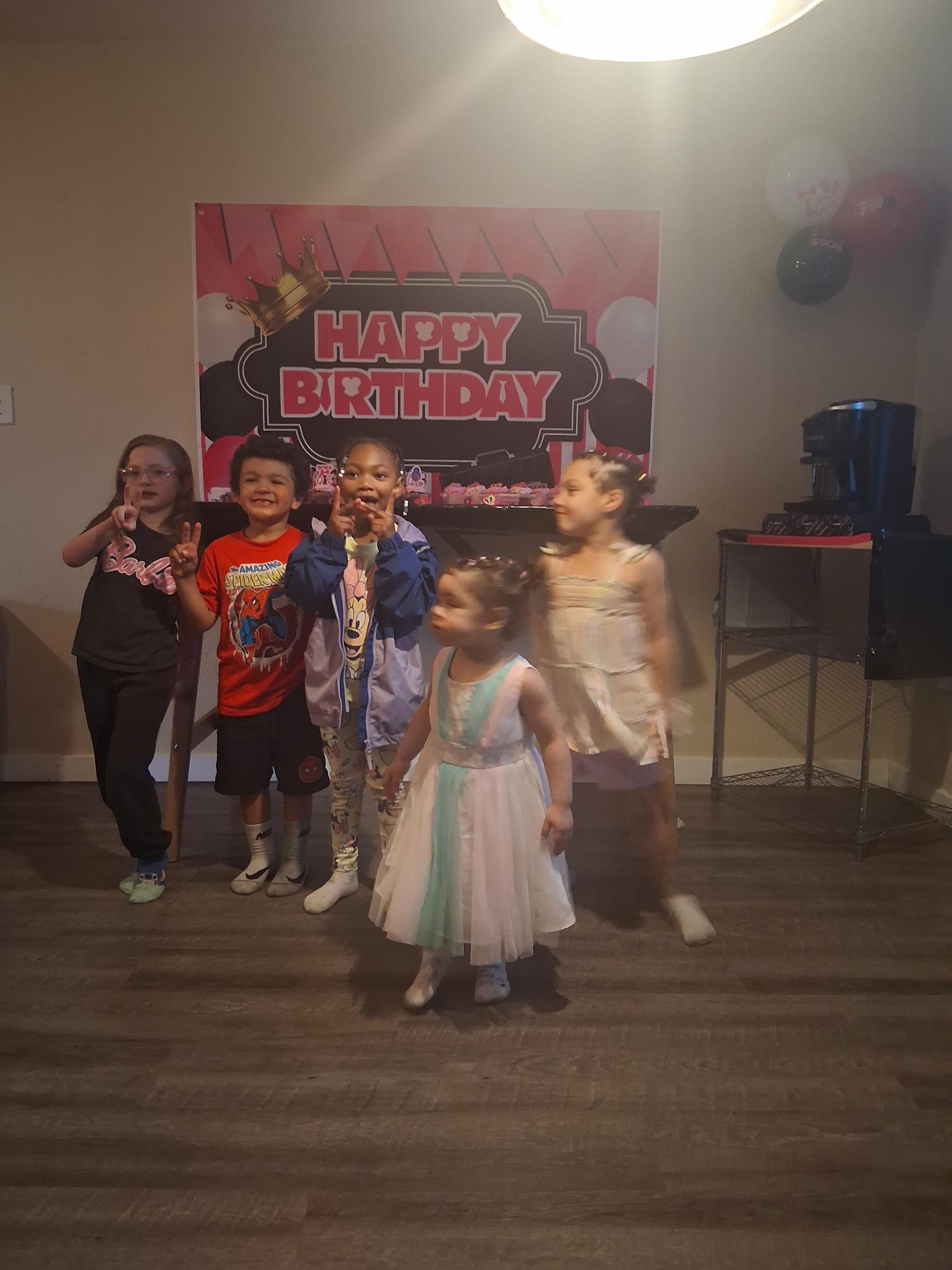 A group of cheerful children celebrate a birthday, posing with excitement near colorful decorations.