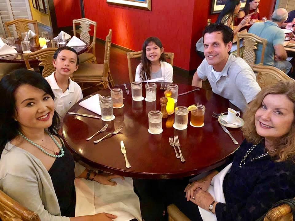 Family gathers at a round table in a restaurant, sharing laughs and enjoying their meal together.