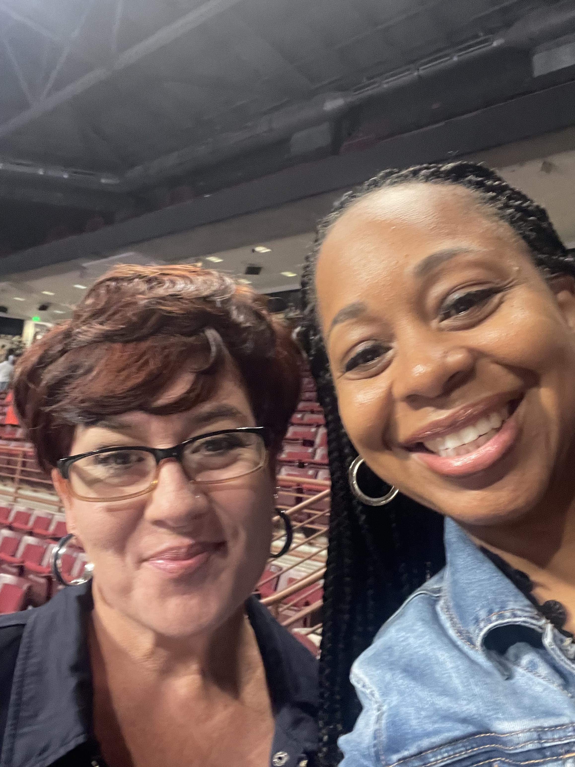 Two friends share smiles while attending an exciting event in a busy arena at night.