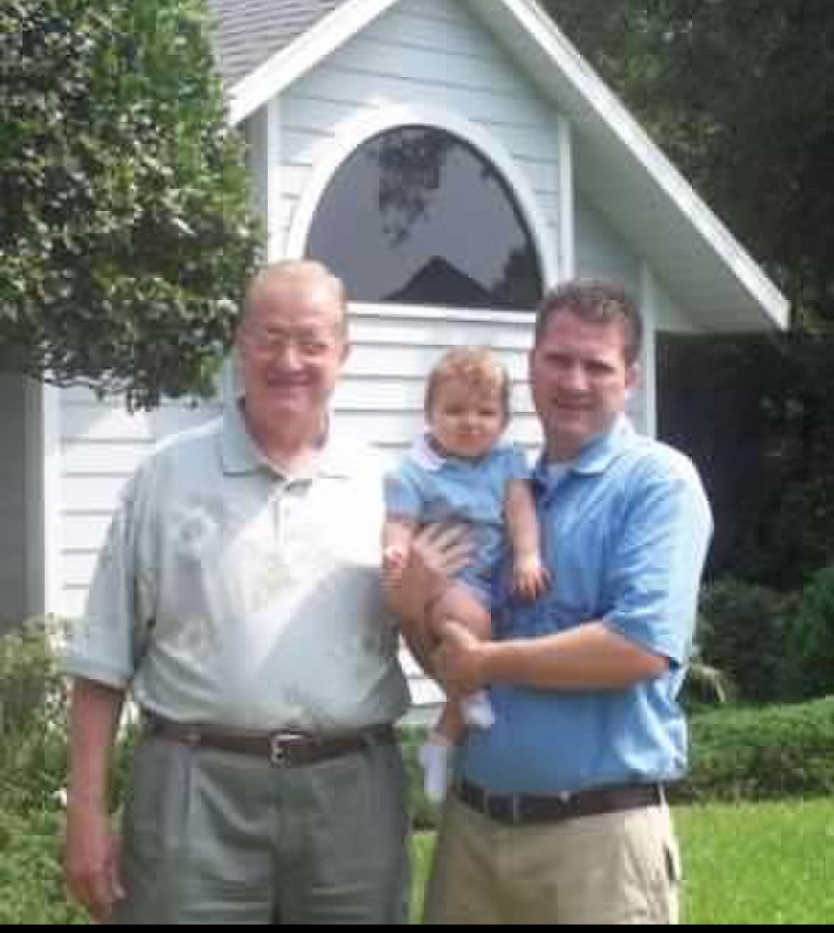 A joyful family stands together outside their home, celebrating a sunny afternoon with a baby.