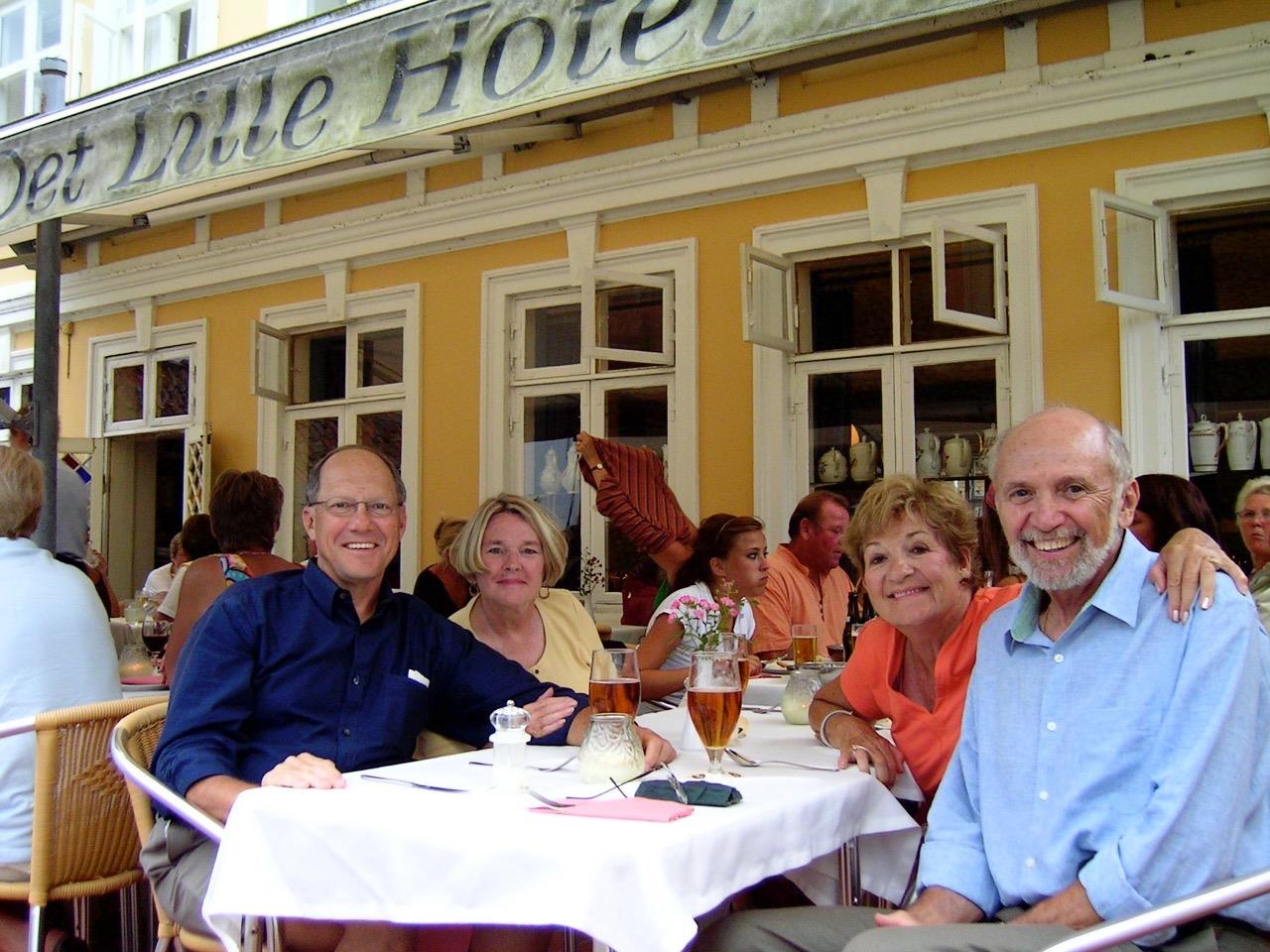 Four friends enjoy a meal together on a hotel terrace, surrounded by a lively atmosphere.