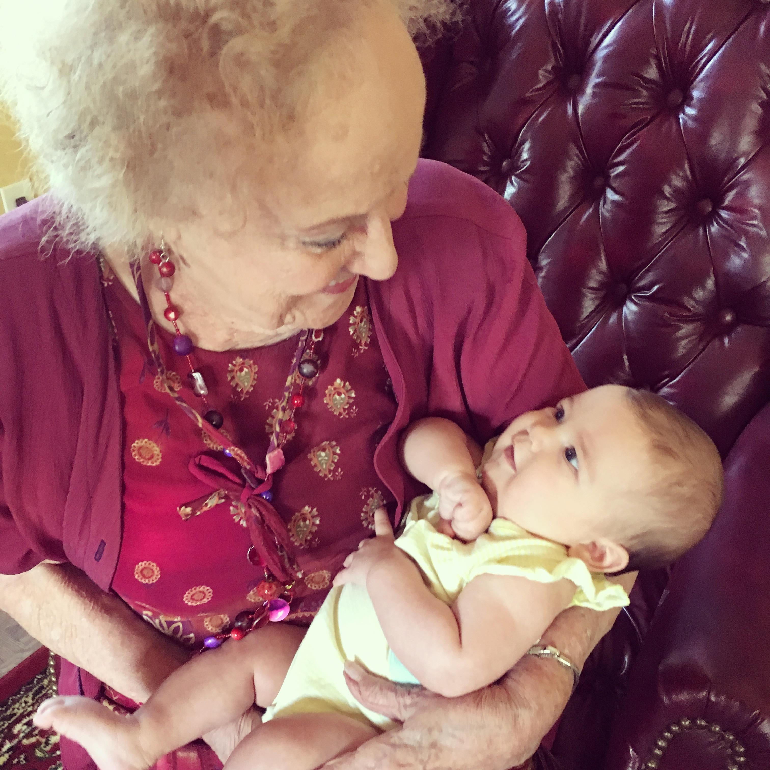 Elderly woman cradles baby in arms, sharing a tender moment in a comfortable living room.