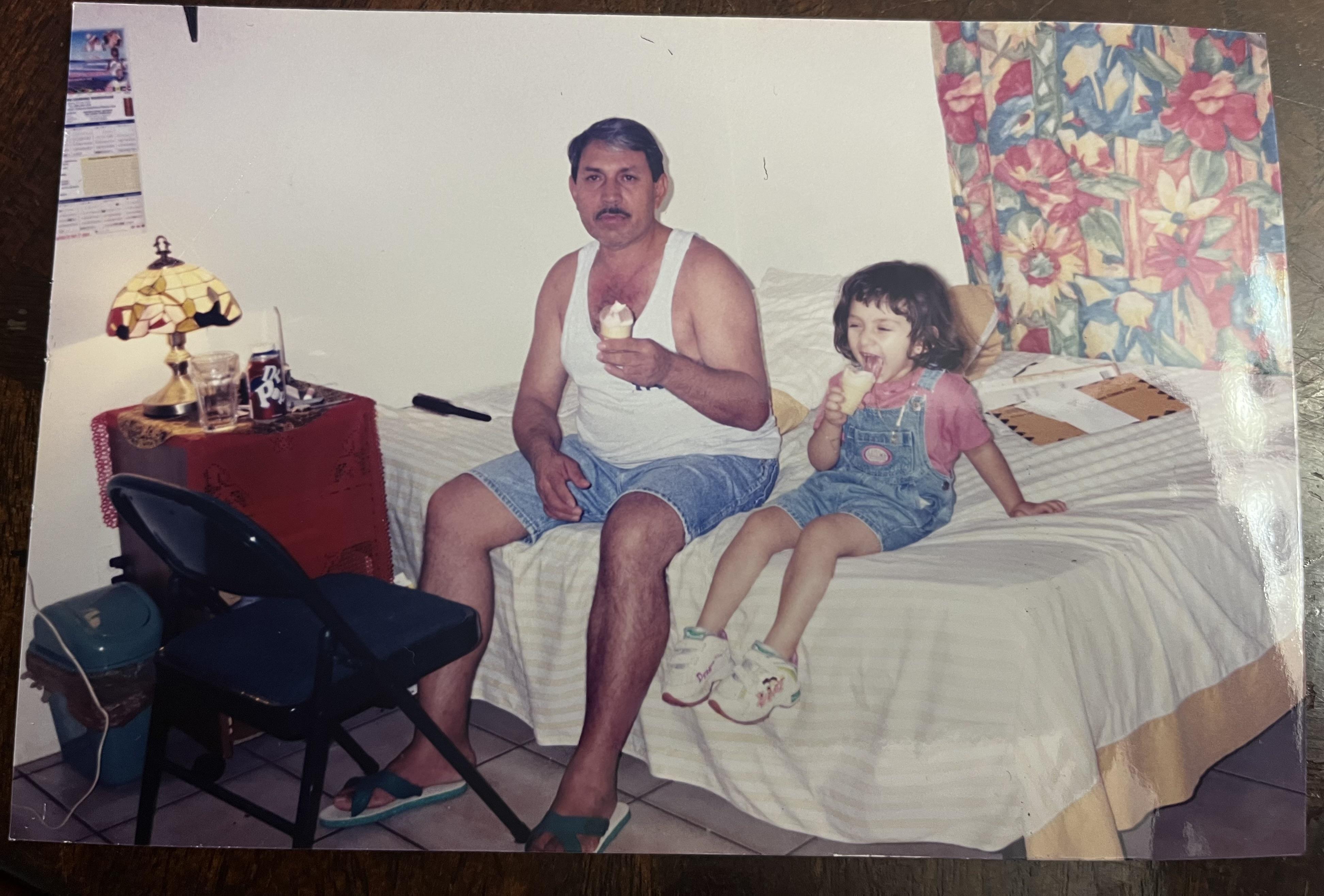 A man and a girl savor ice cream while sitting on a bed with a colorful floral backdrop.