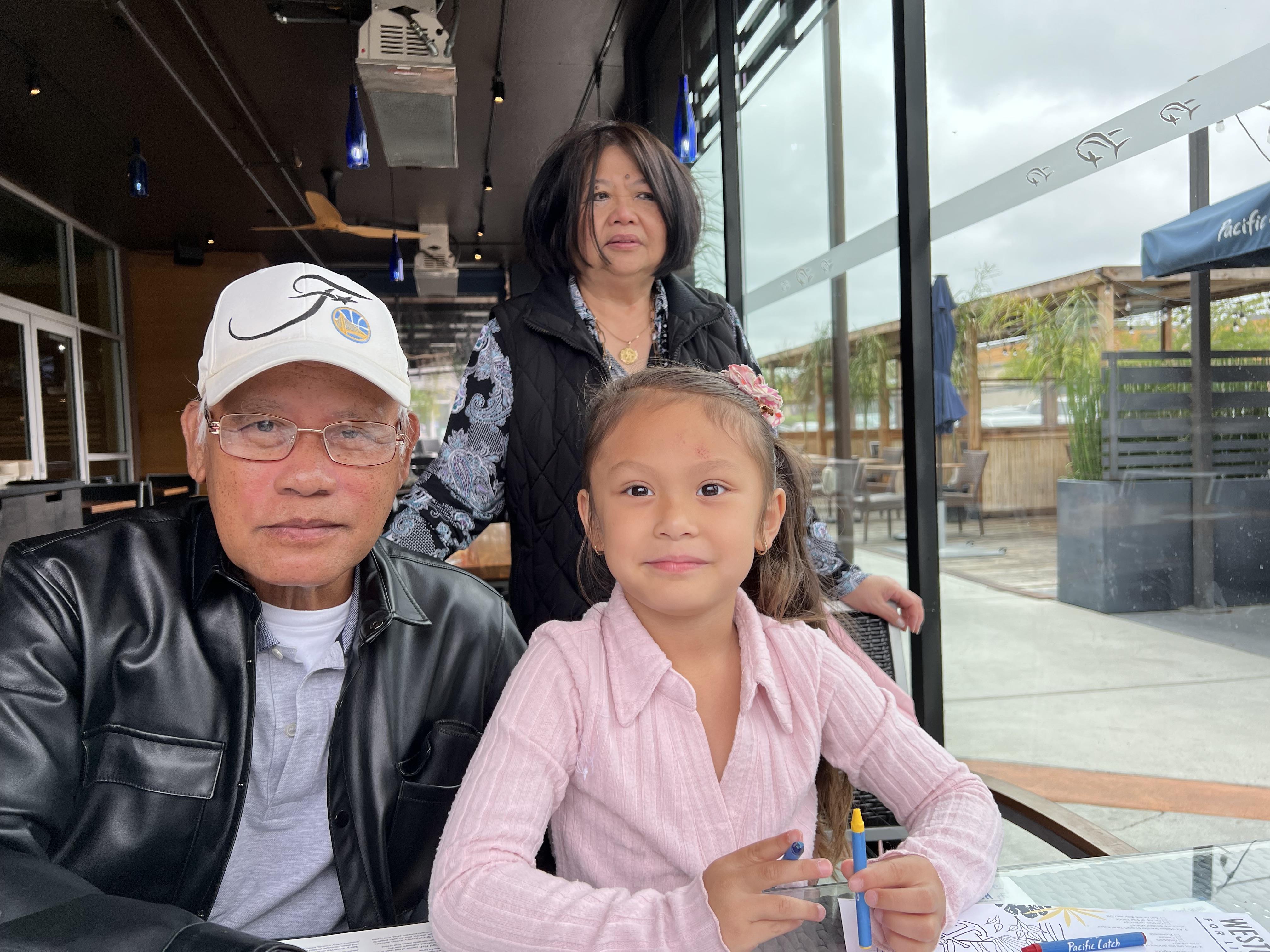 A young girl and an elderly man share a table with a woman in a casual dining setting.