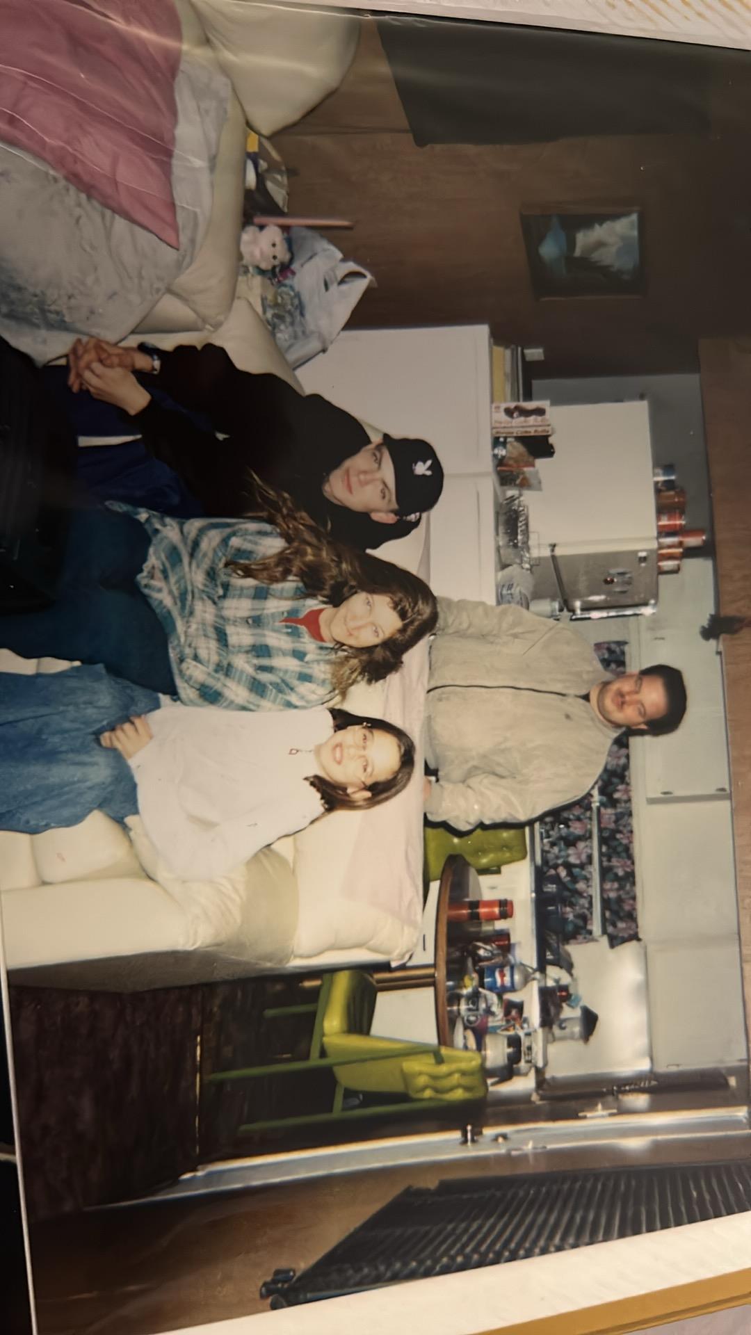Four friends gather on a sofa in a cozy apartment, enjoying time together in winter attire.