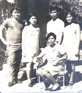 Five friends gather outside a house, dressed casually, smiling and enjoying their time together.