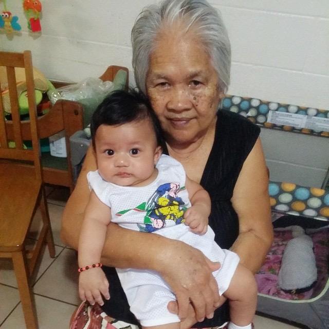 A grandmother smiles while holding her baby grandchild in a warm and inviting space.