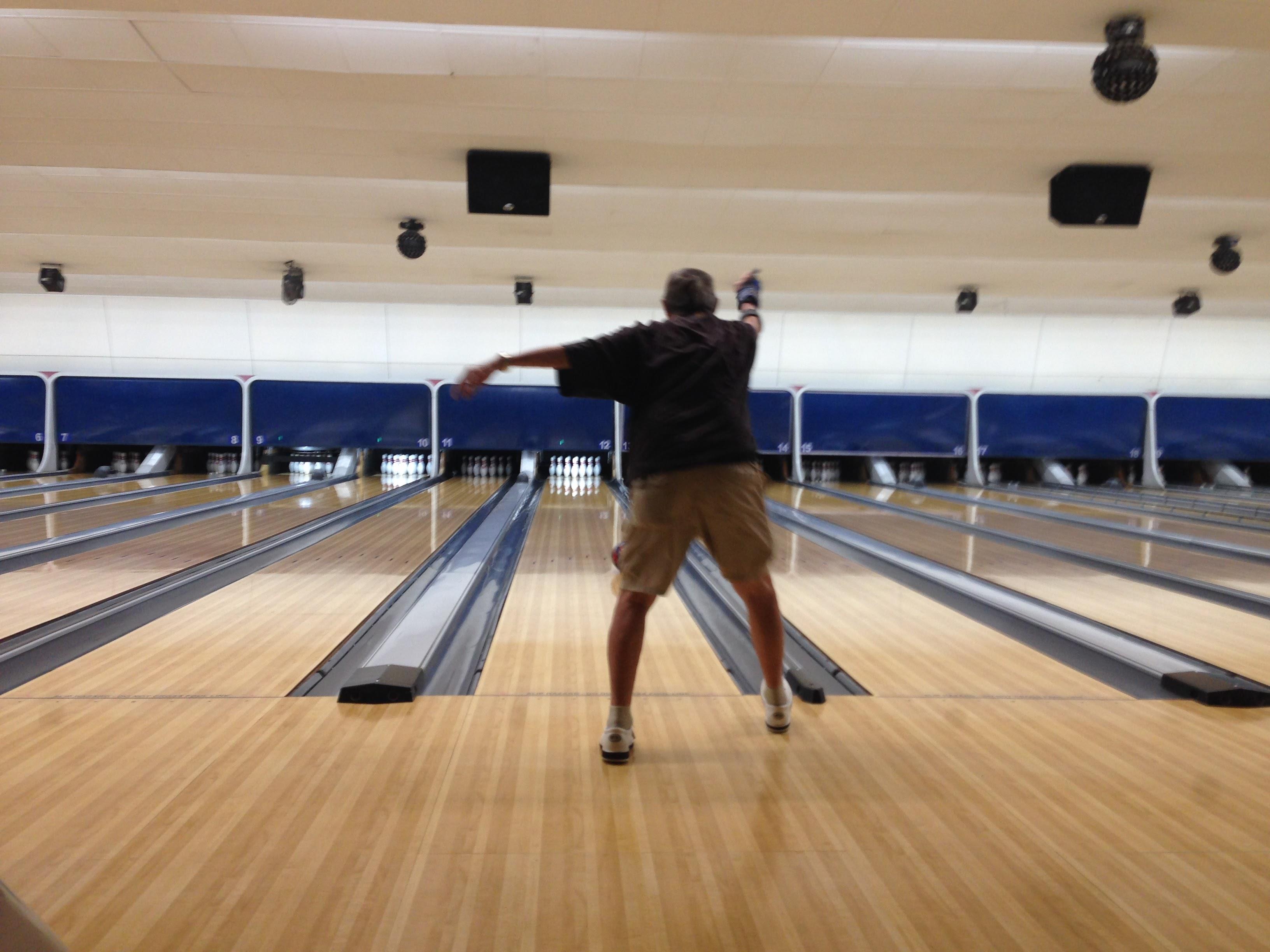 A bowler releases their ball towards the pins in a spacious bowling alley.