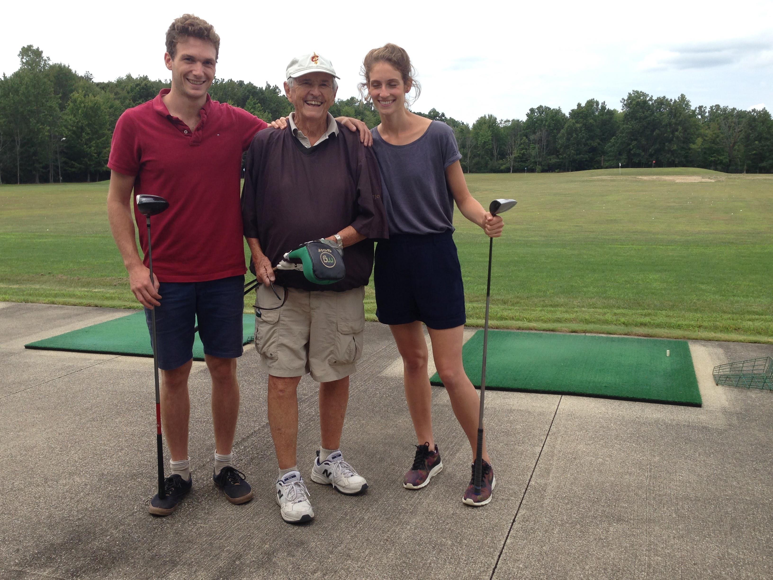 Three individuals enjoy a sunny afternoon practicing golf swings at a driving range.