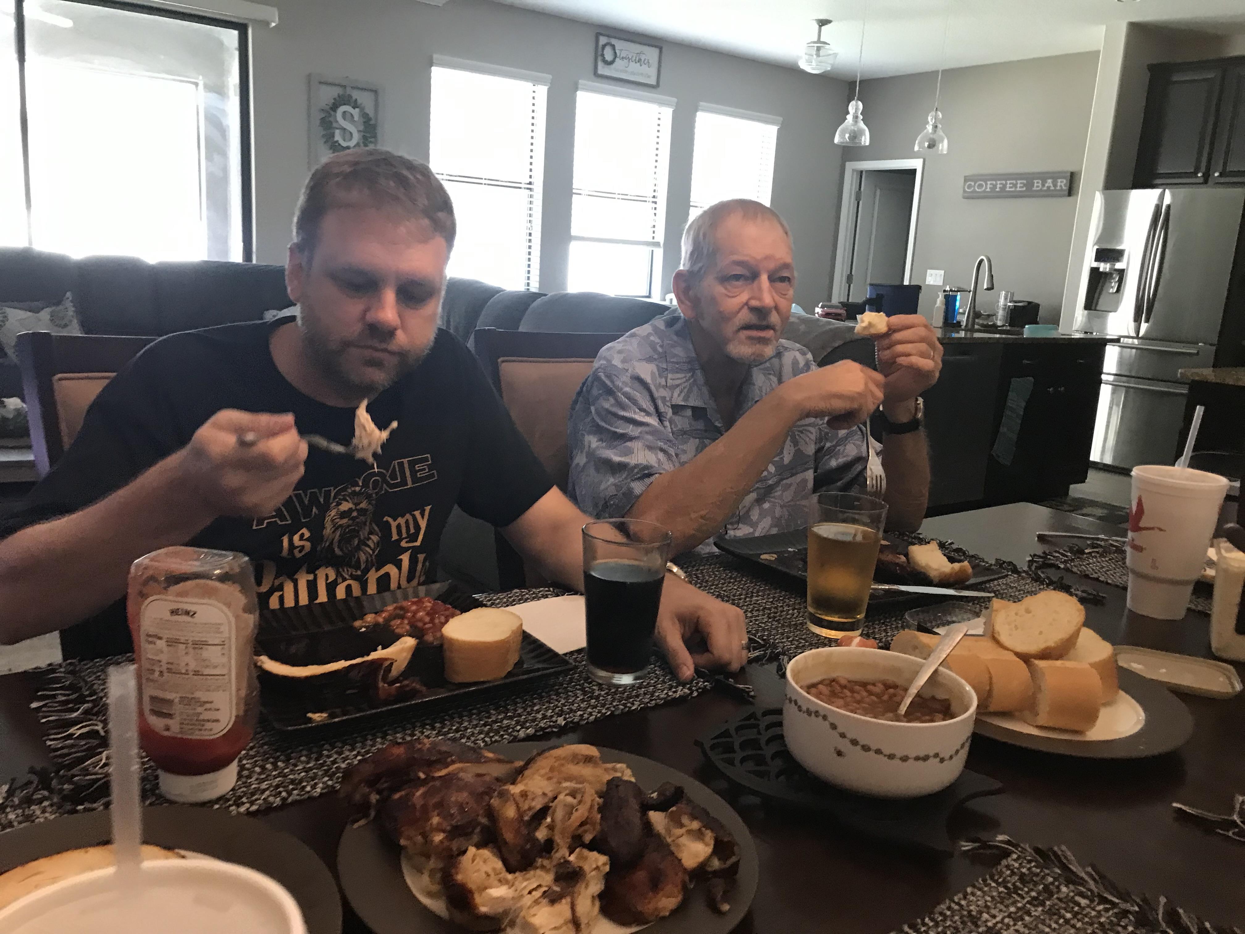 Friends share a delicious lunch featuring barbecue chicken, sides, and drinks in a cozy kitchen.