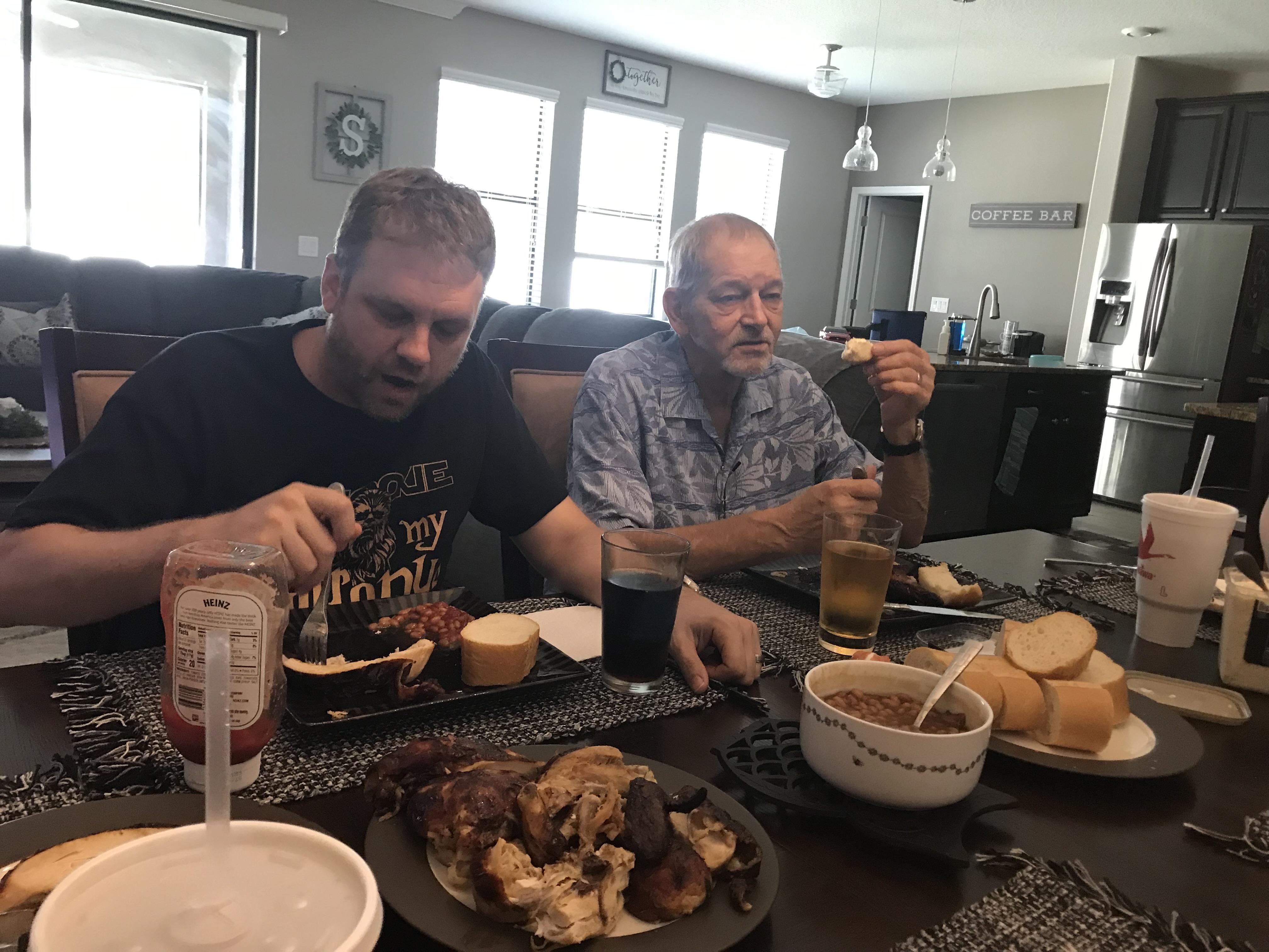 Two men enjoy a delicious barbecue meal at a dining table in a cozy home setting.