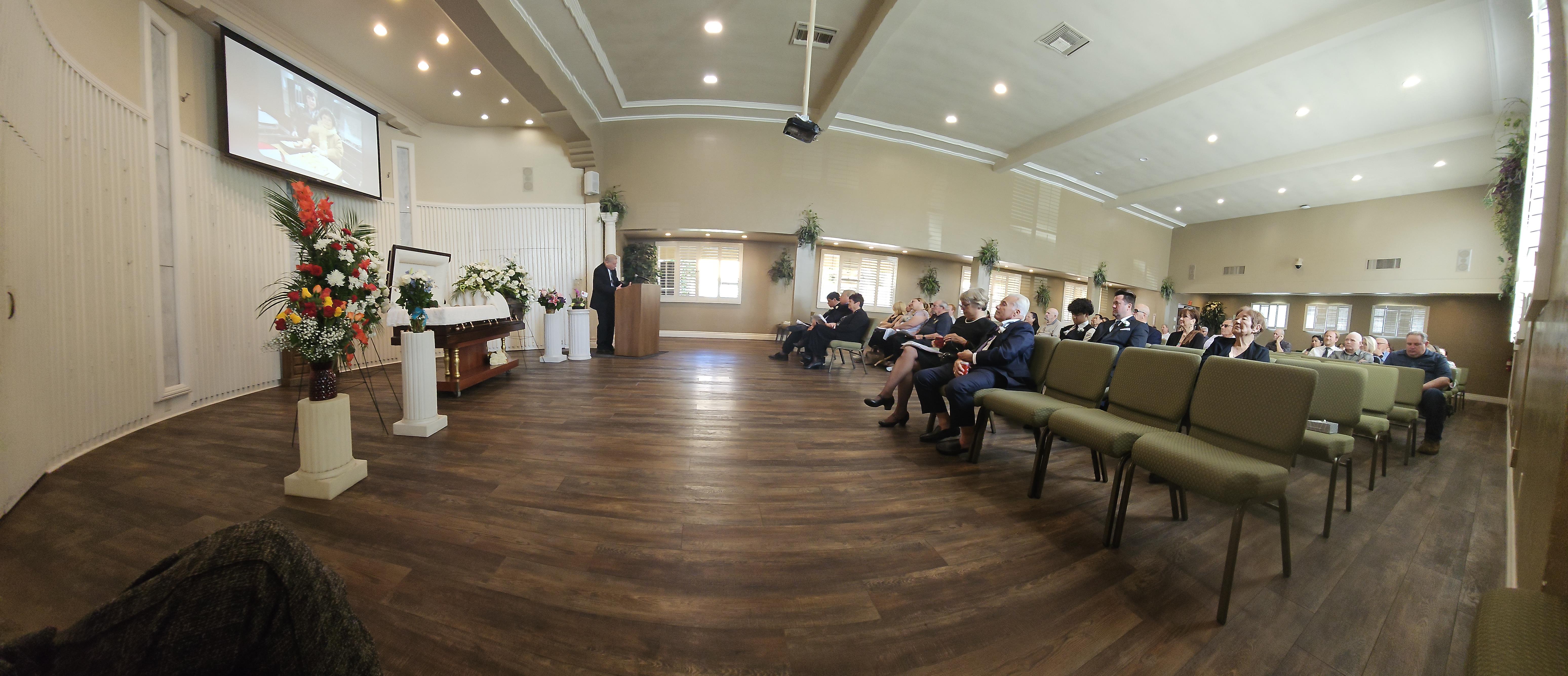 Attendees gather in a hall, listening to a speaker at a podium during a somber memorial event.