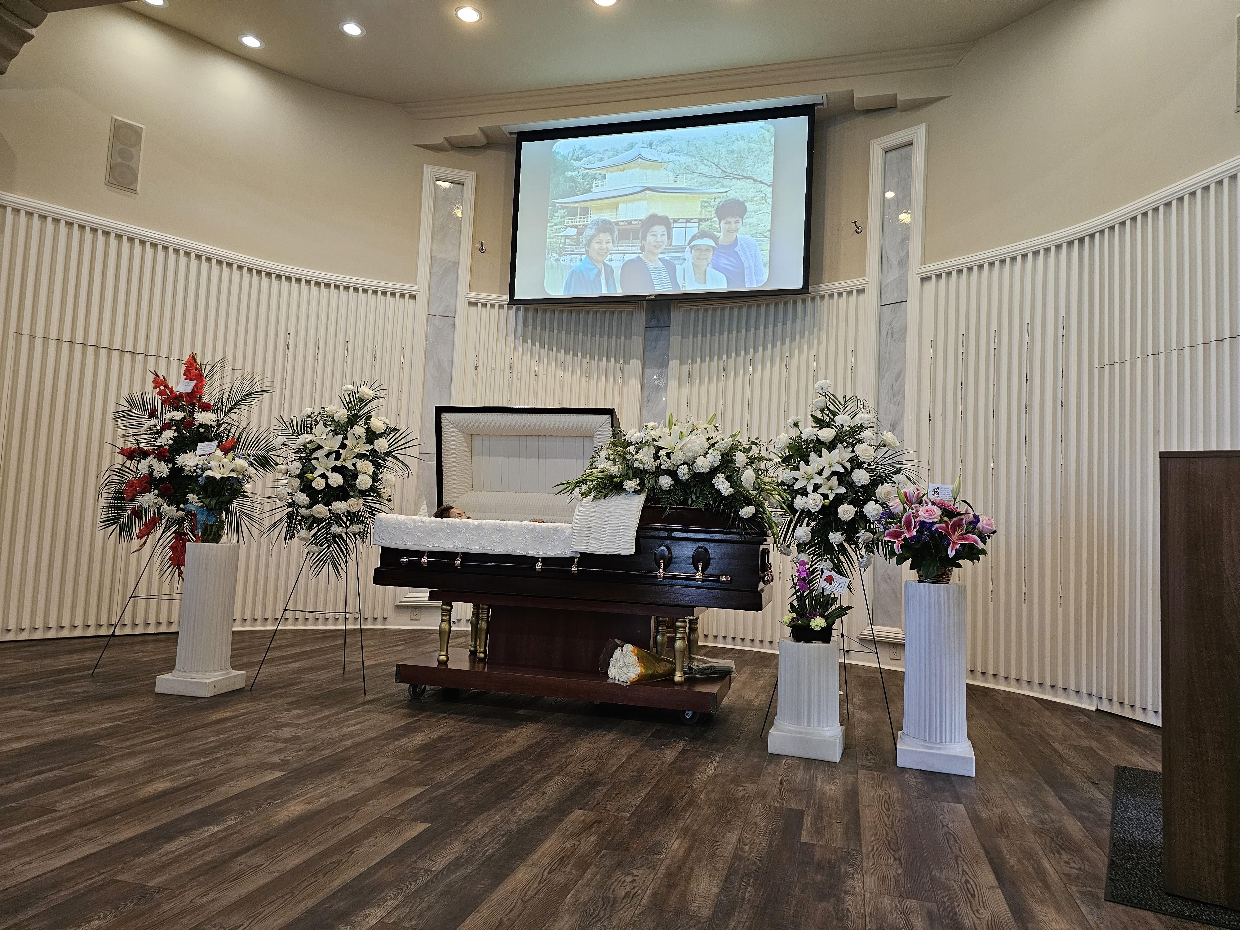 A solemn memorial service is set up in a serene environment with flowers and a tribute screen.