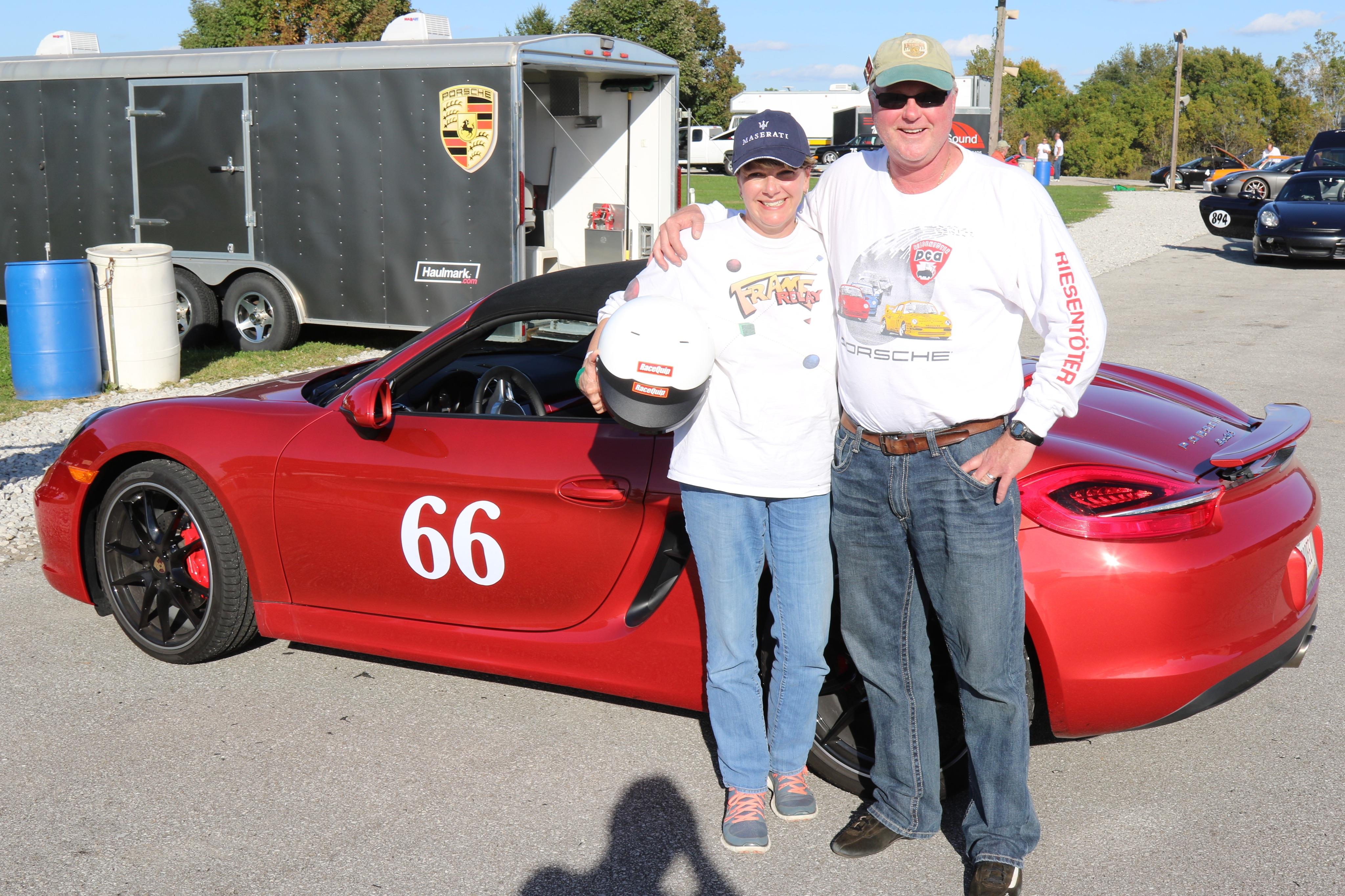 A couple poses proudly with a red sports car, showcasing their excitement after racing.