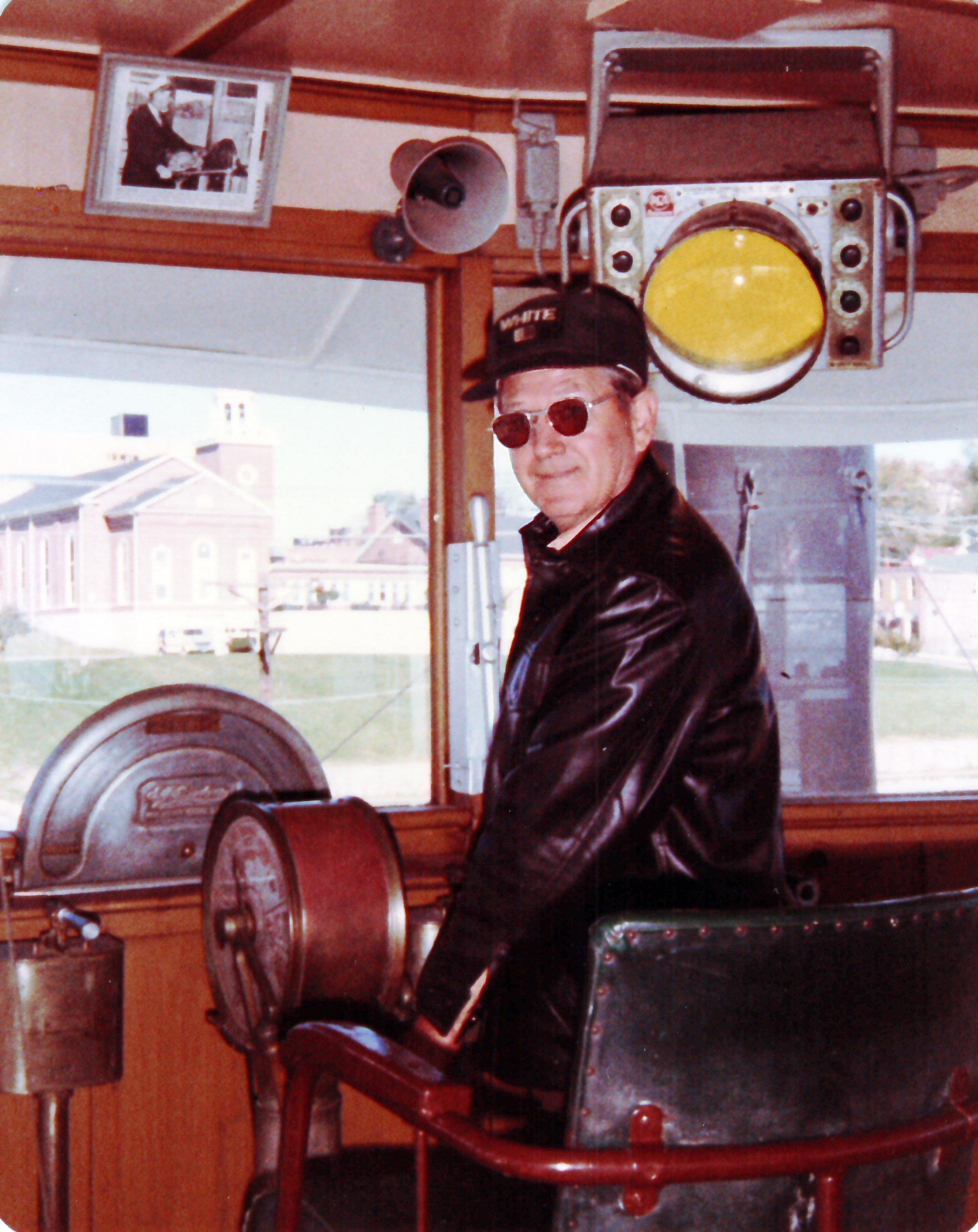 Man navigates a classic vessel from the control room in a serene harbor.