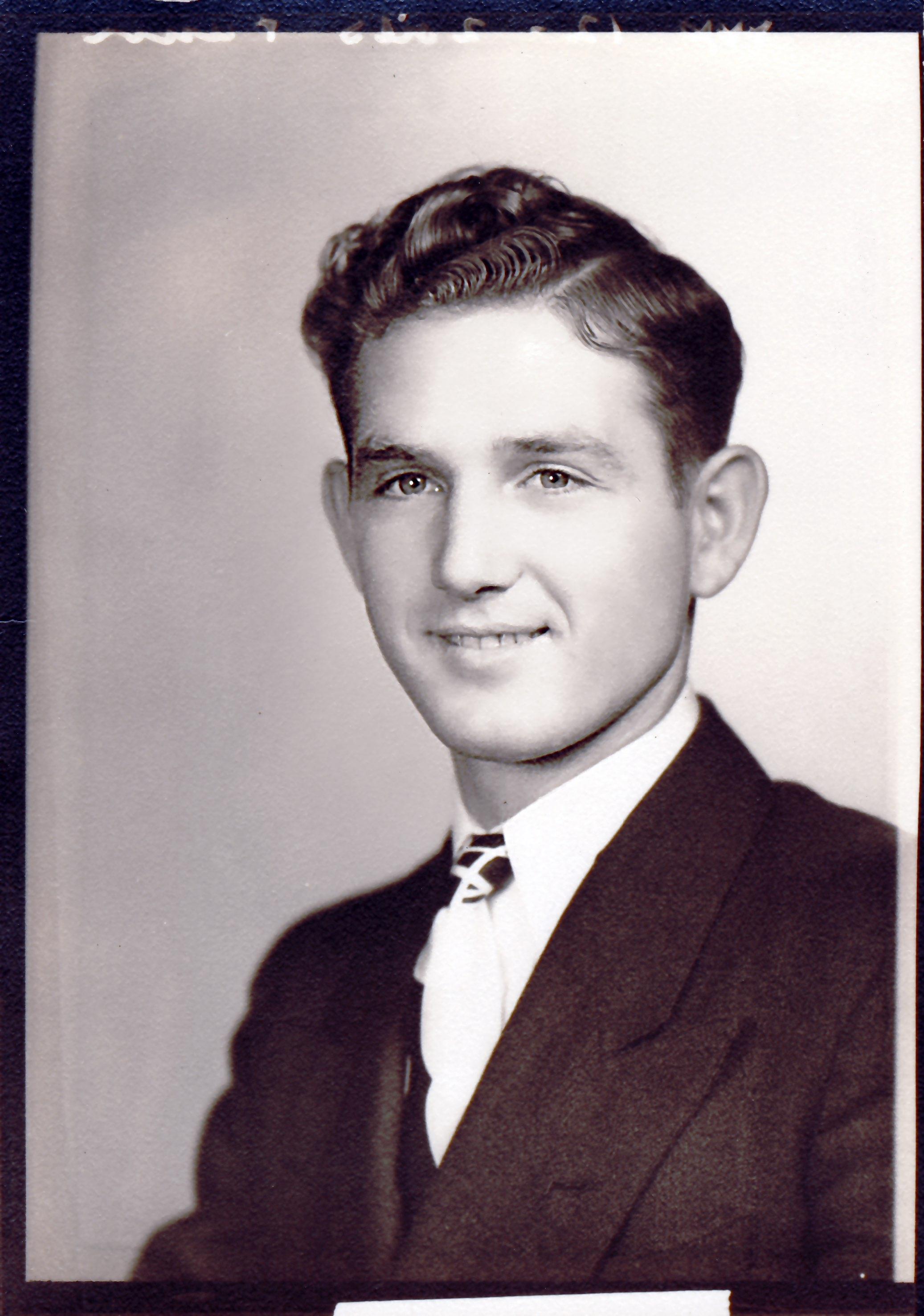 Young man dressed in a suit and tie smiles confidently while posing for a portrait.