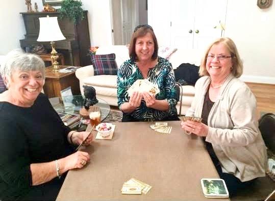 Three friends gather around a table, engaged in a lively card game while laughing.