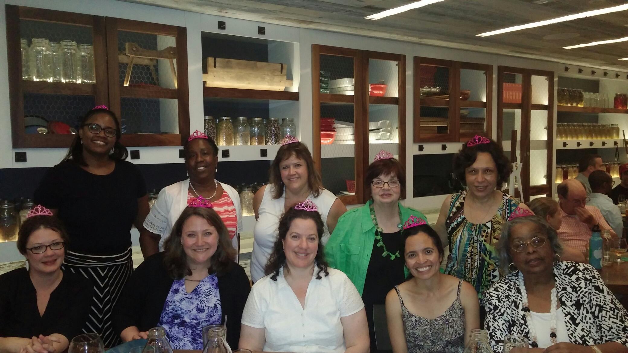Friends gather around a table in a lively restaurant, wearing tiaras and enjoying the celebration.