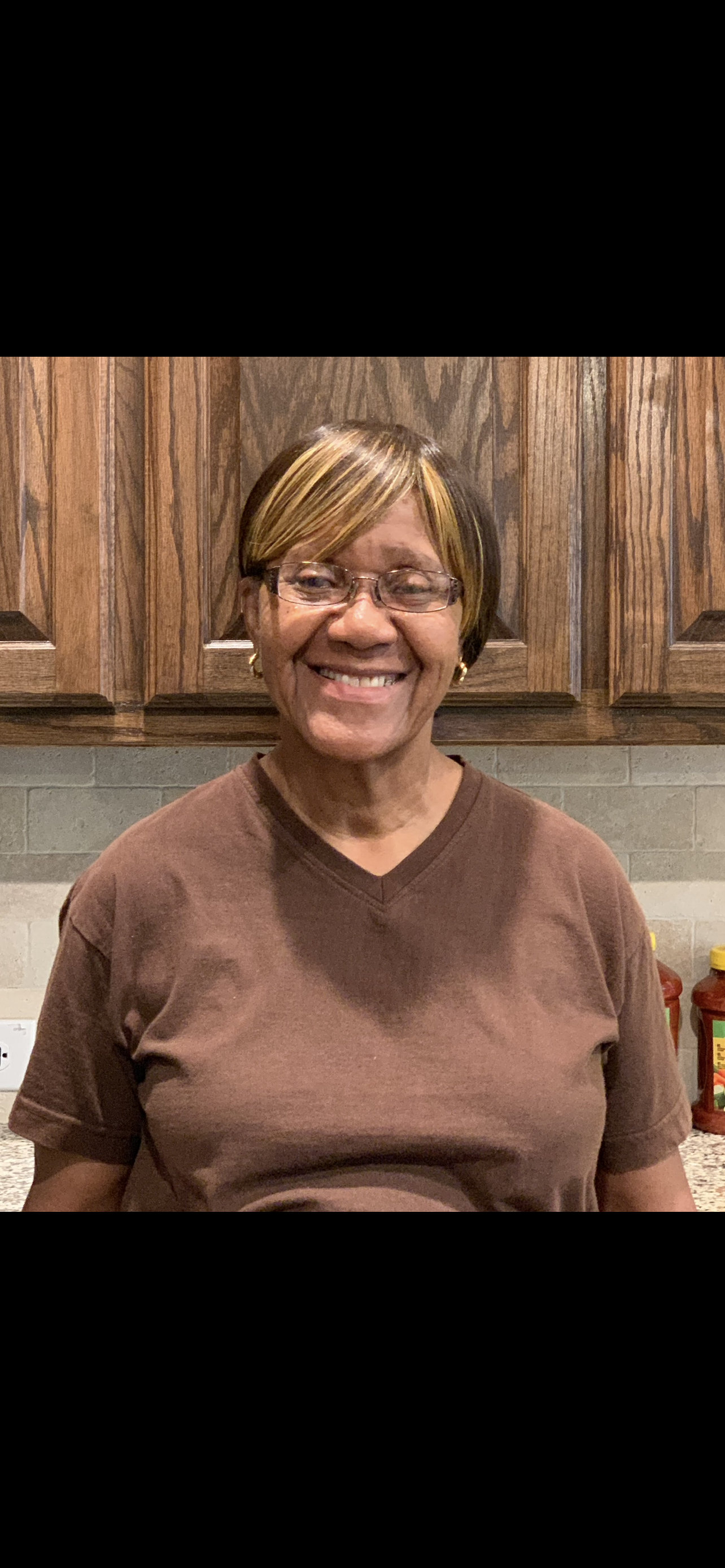 An elderly woman stands in a cozy kitchen, smiling and exuding warmth and happiness.