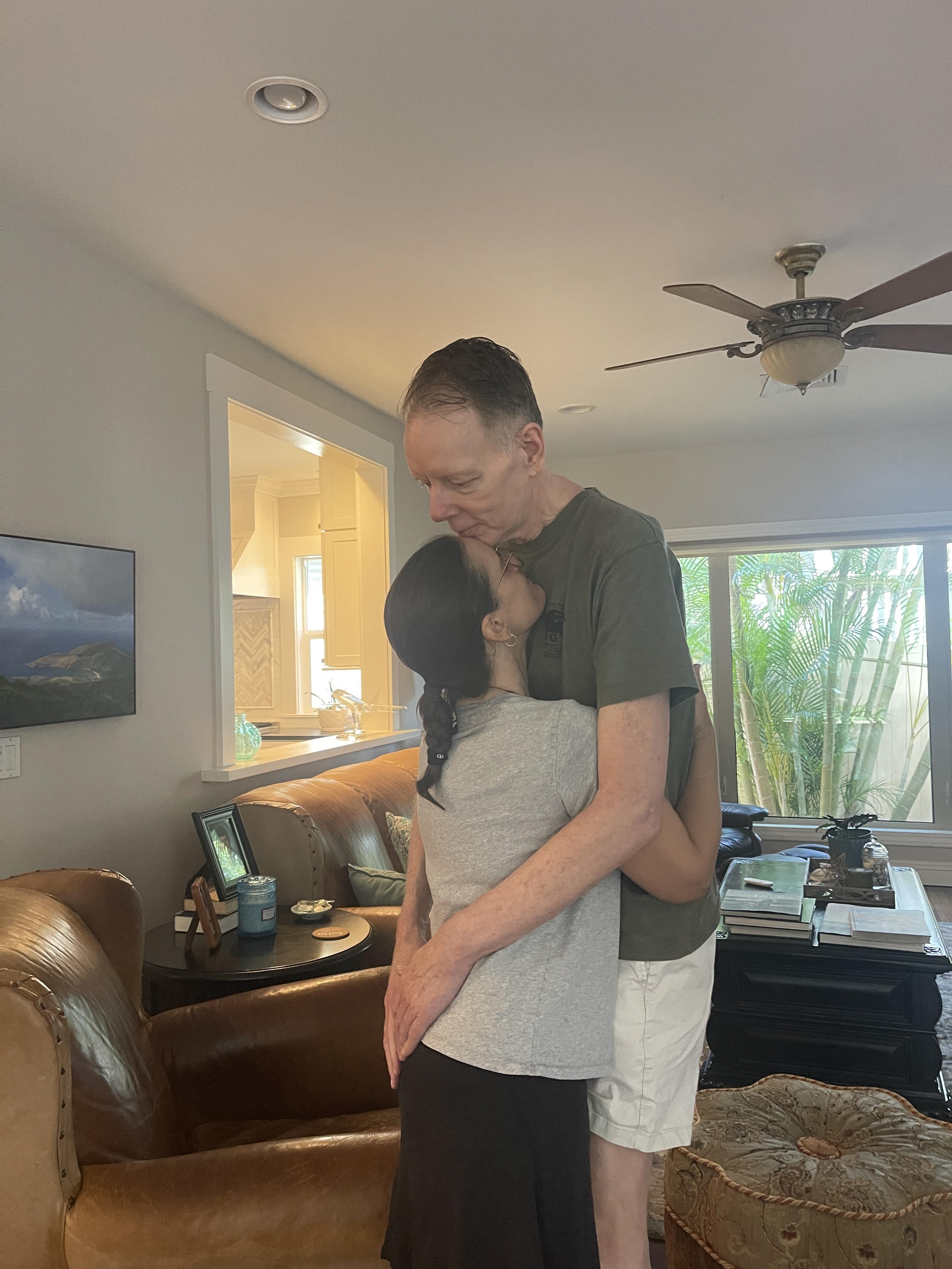A man and woman embrace in a warm and loving hug in their comfortable living room.