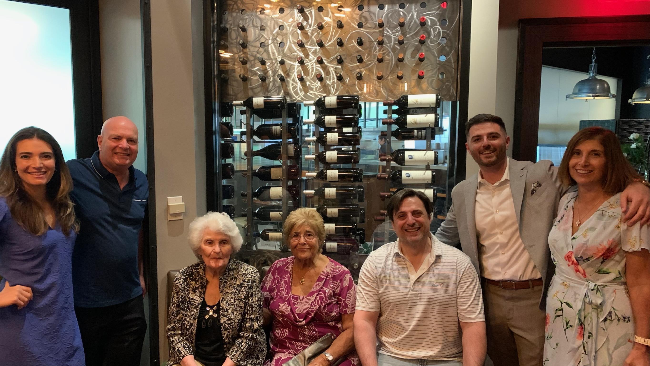 A joyful family gathers for a special occasion beside an impressive wine collection.