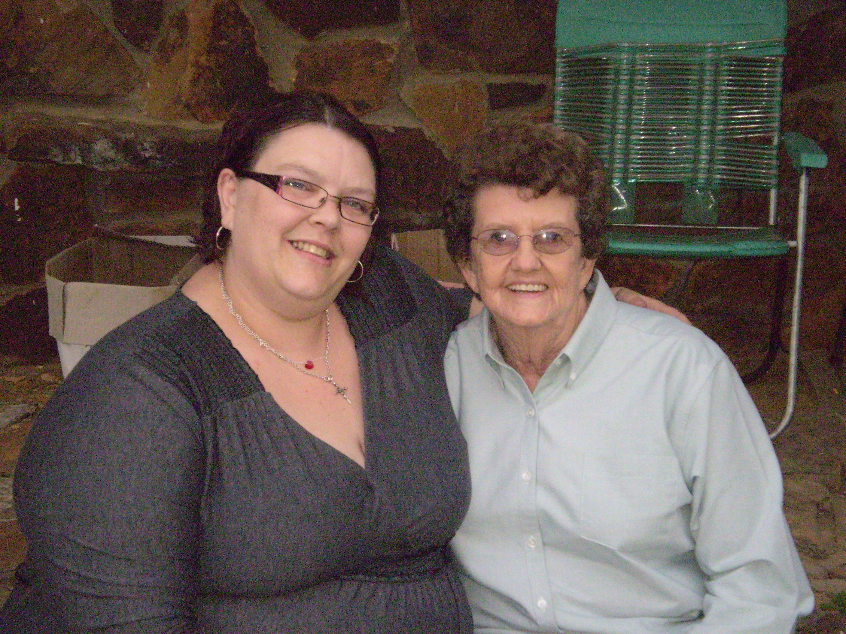 Two women smile warmly while seated in a cozy gathering, sharing a special moment together.