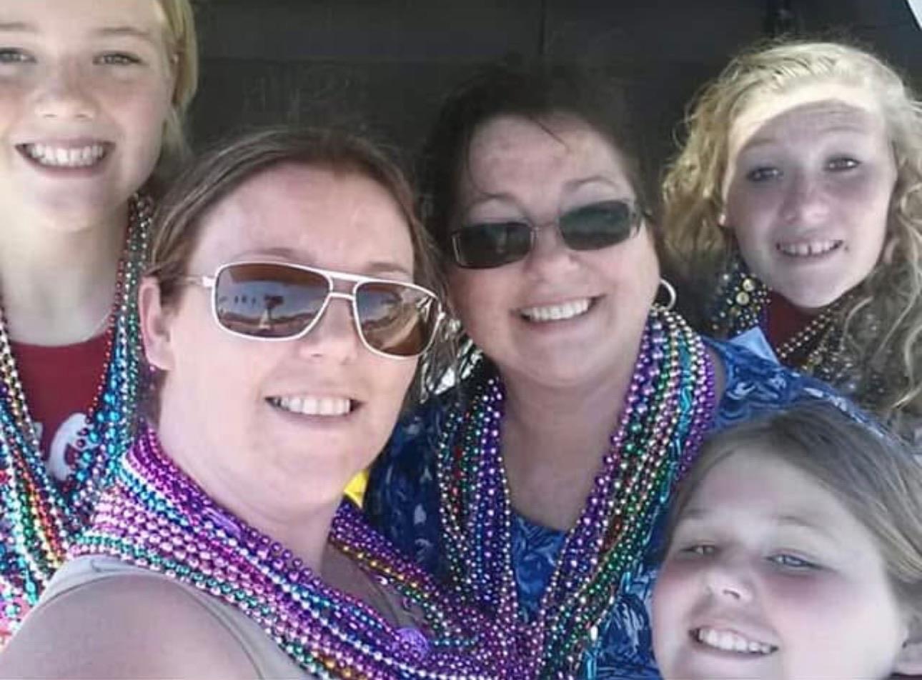 Group of women and girls celebrating Mardi Gras with vibrant beads and joyful smiles together.