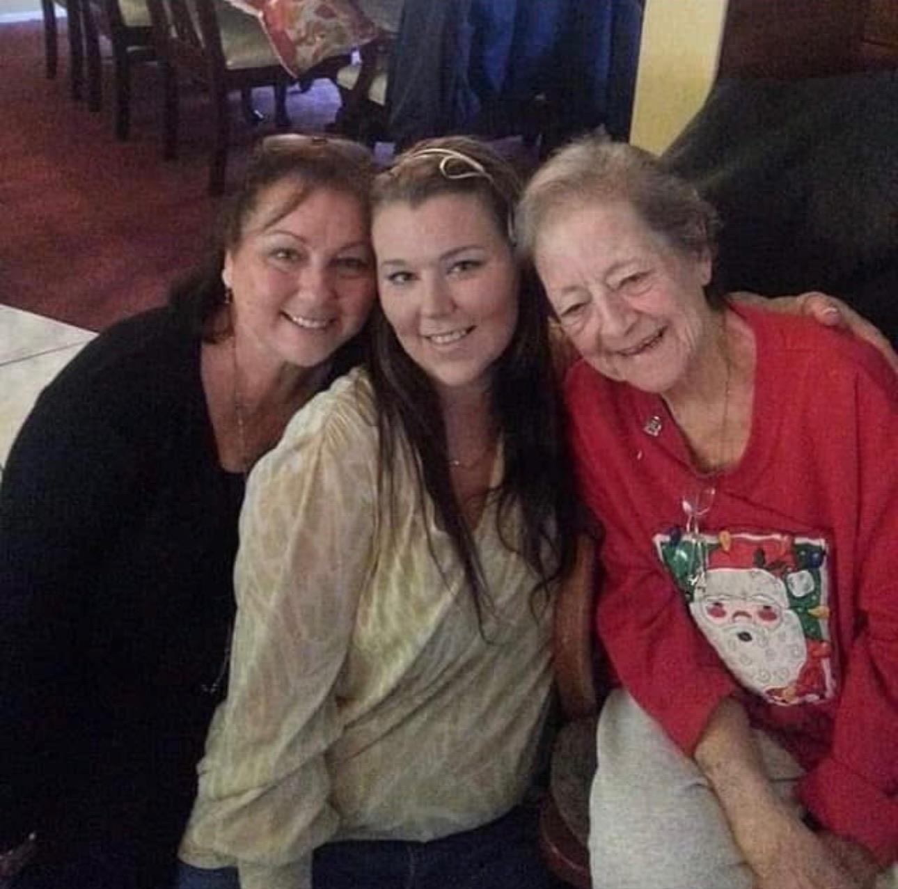 Three women share smiles and laughter together in a cozy living room during the holidays.