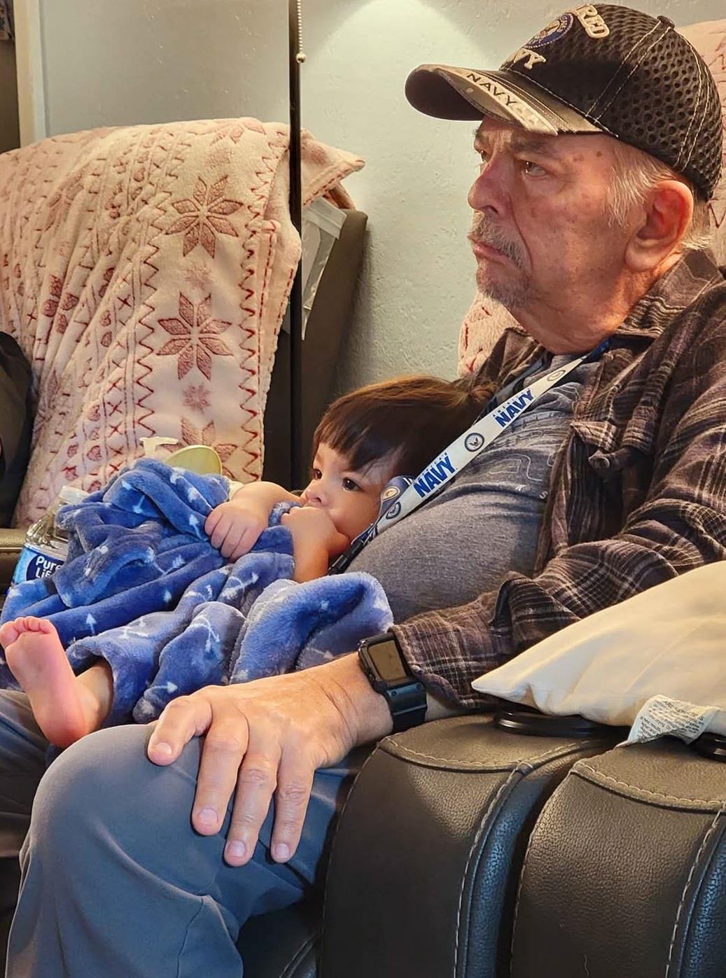 A grandfather and his grandson sit together, relaxed and watching TV in a cozy living room.