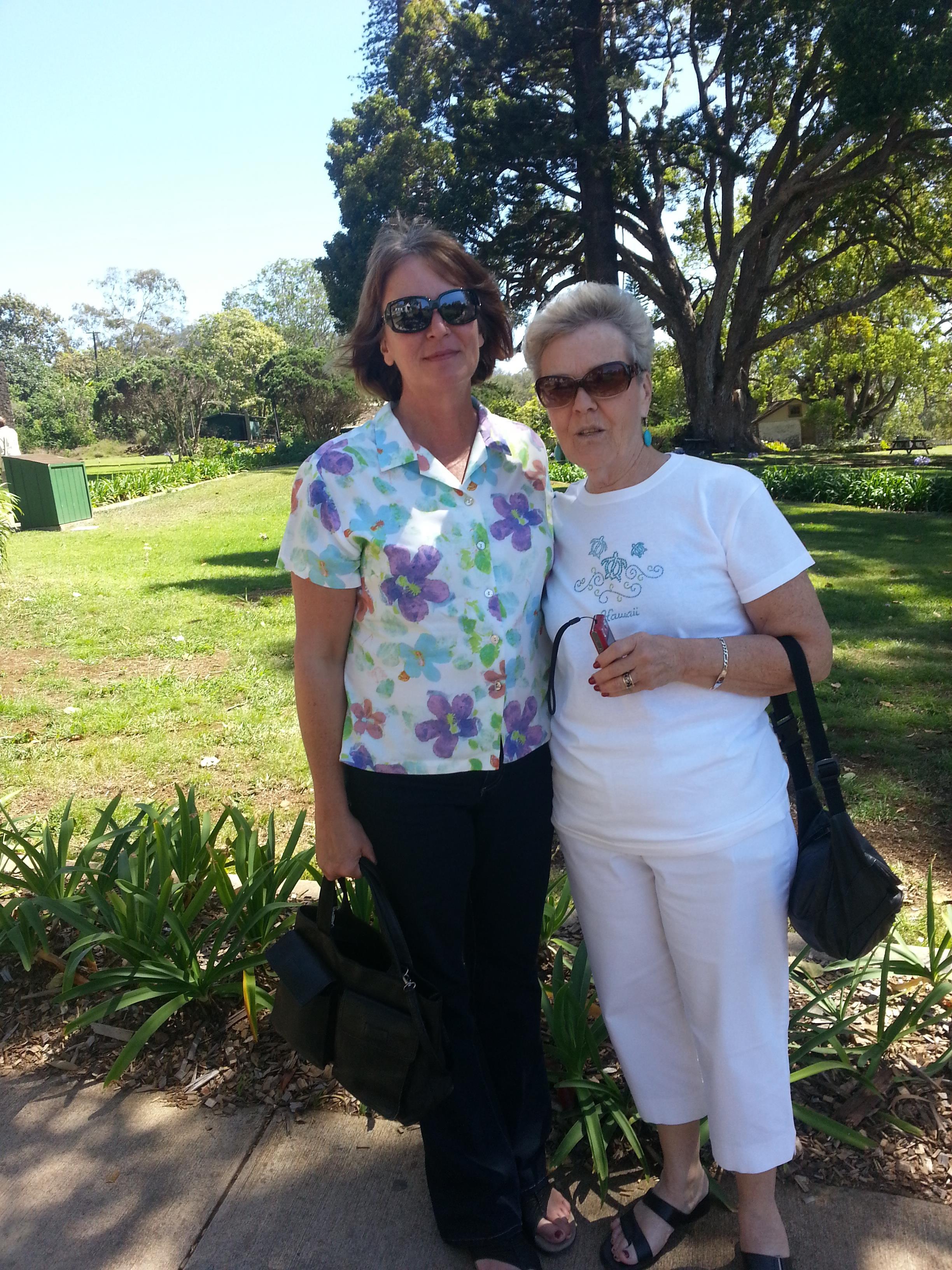 Two women stand together in a vibrant garden, smiling under the bright sun on a clear day.