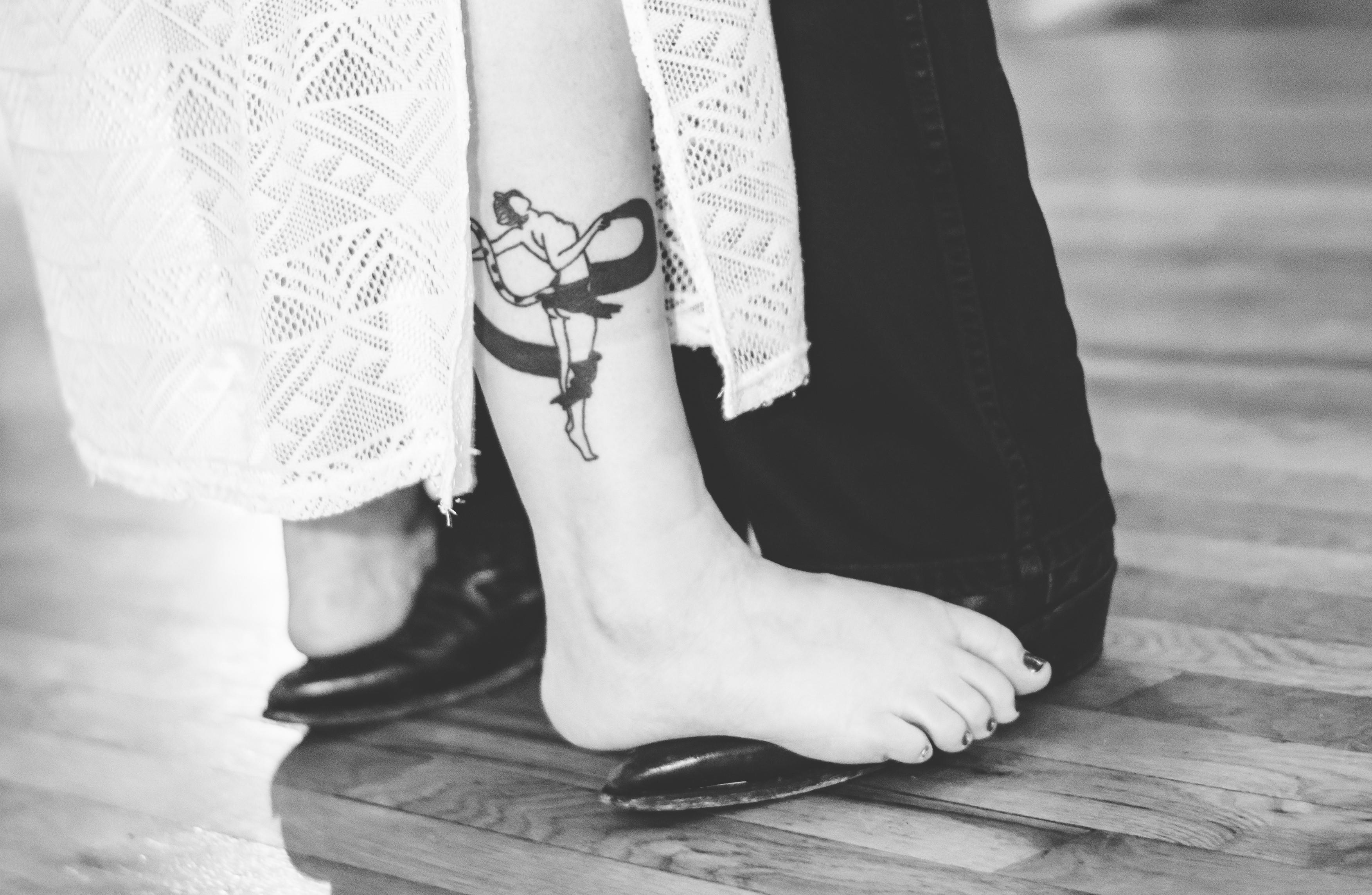 Tattoo of a dancer is visible on the leg while wearing sandals at home.
